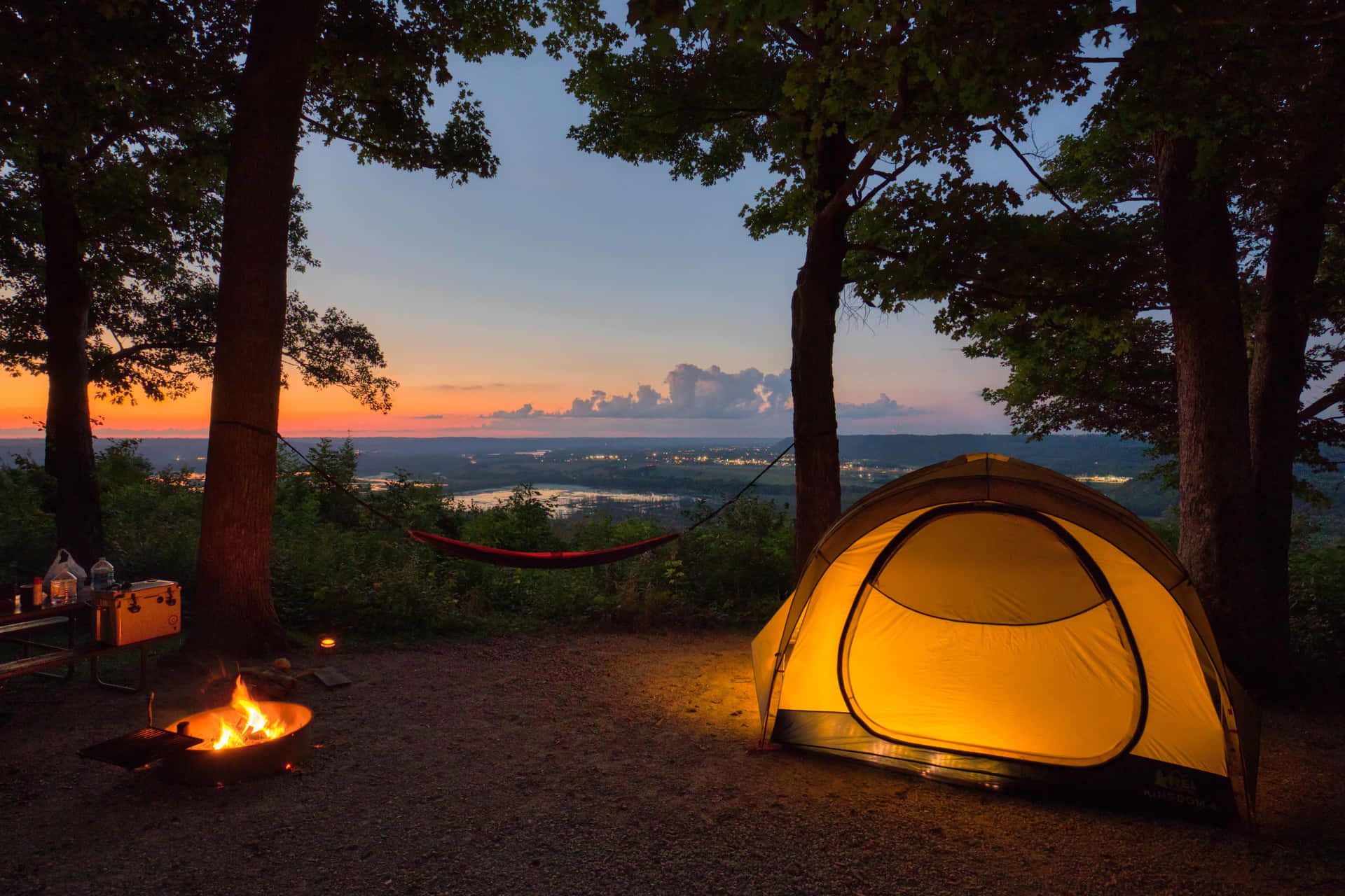 A tent and campfire overlooking a scenic view at sunset. - Camping