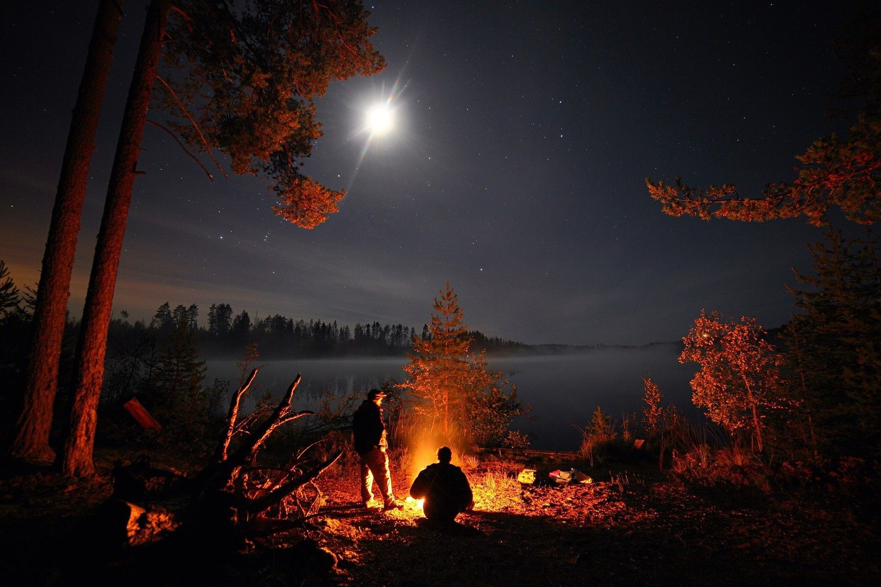 People sitting around a campfire under a full moon - Camping