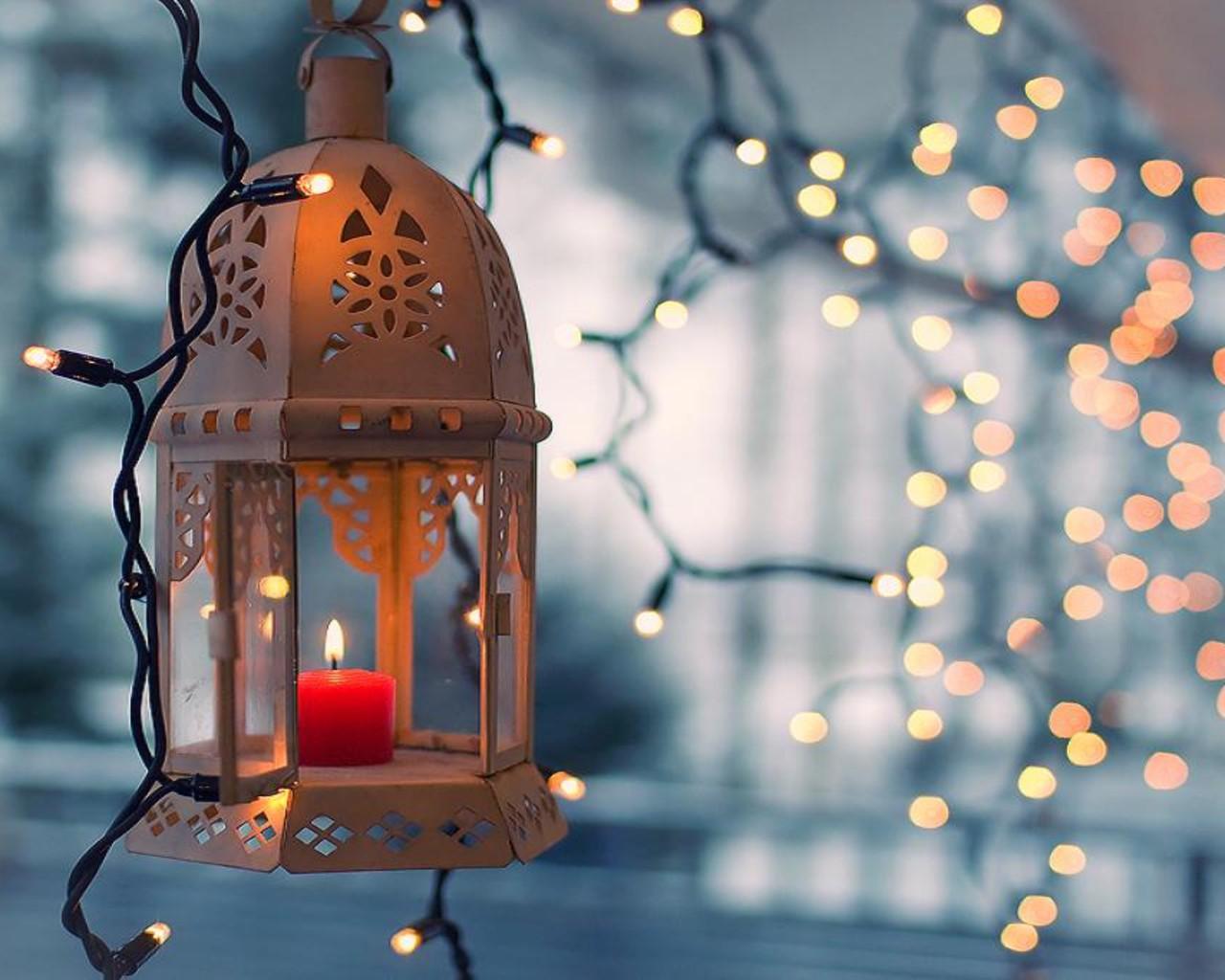 A red candle in a lantern with fairy lights in the background. - Fairy lights