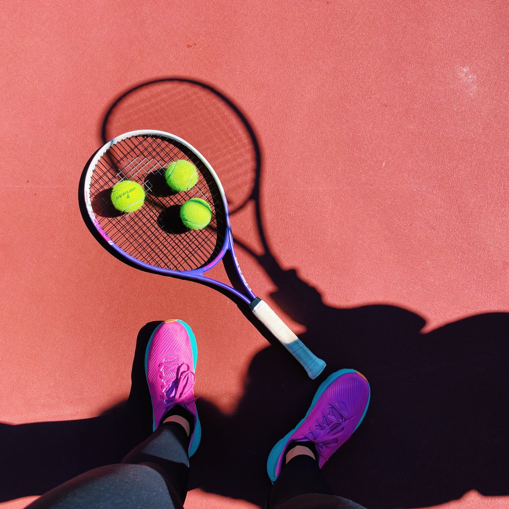 A tennis racket with two tennis balls on a red surface. - Tennis