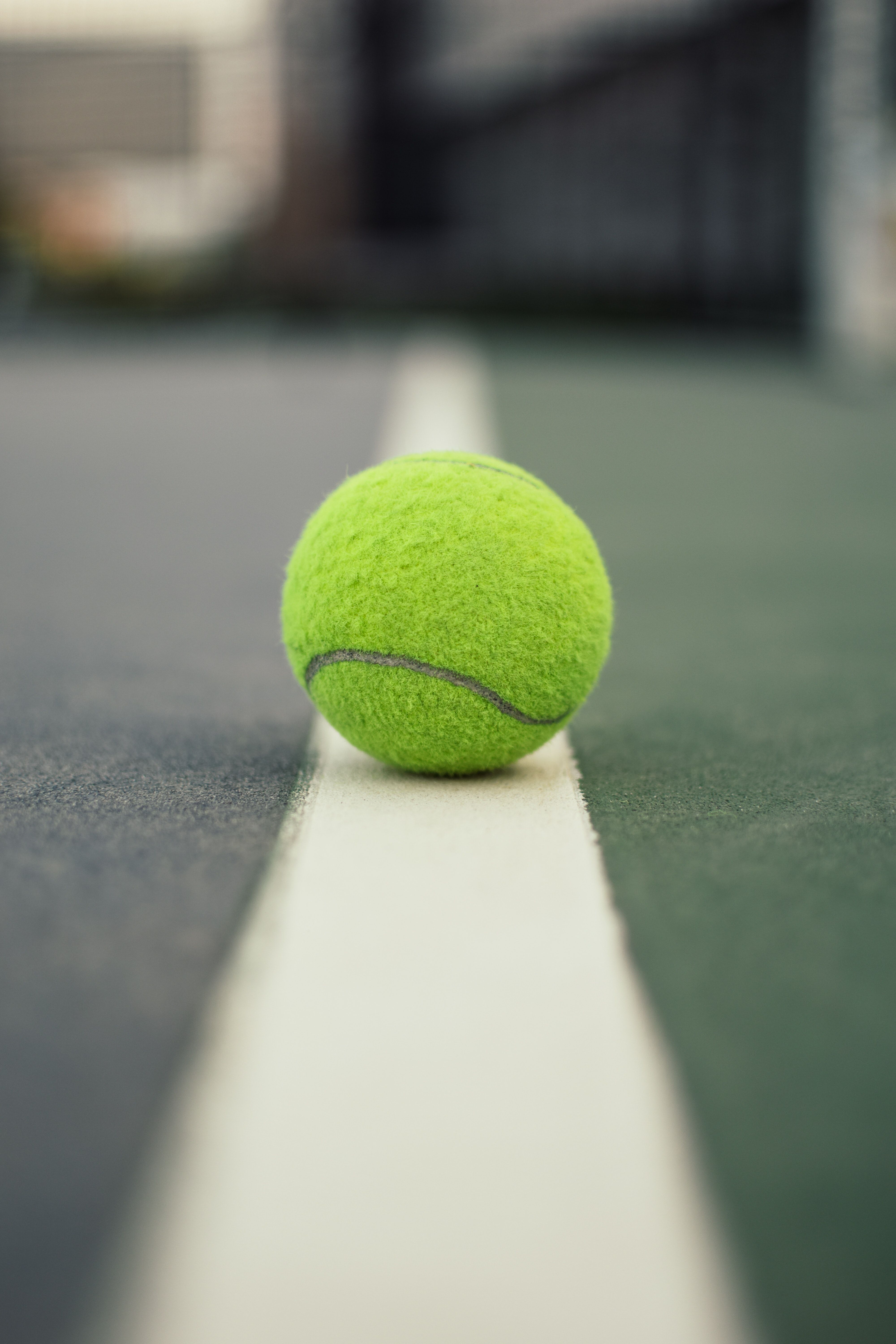 A tennis ball sitting on the edge of an outdoor court - Tennis