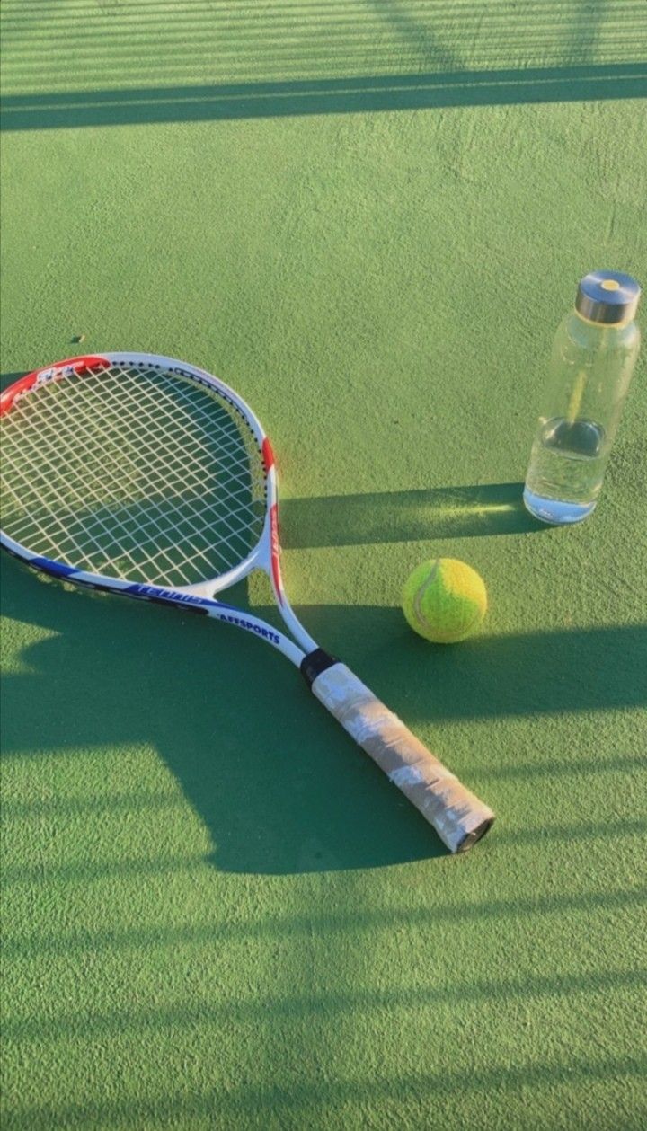 A tennis racket, tennis ball, and water bottle sit on a tennis court. - Tennis