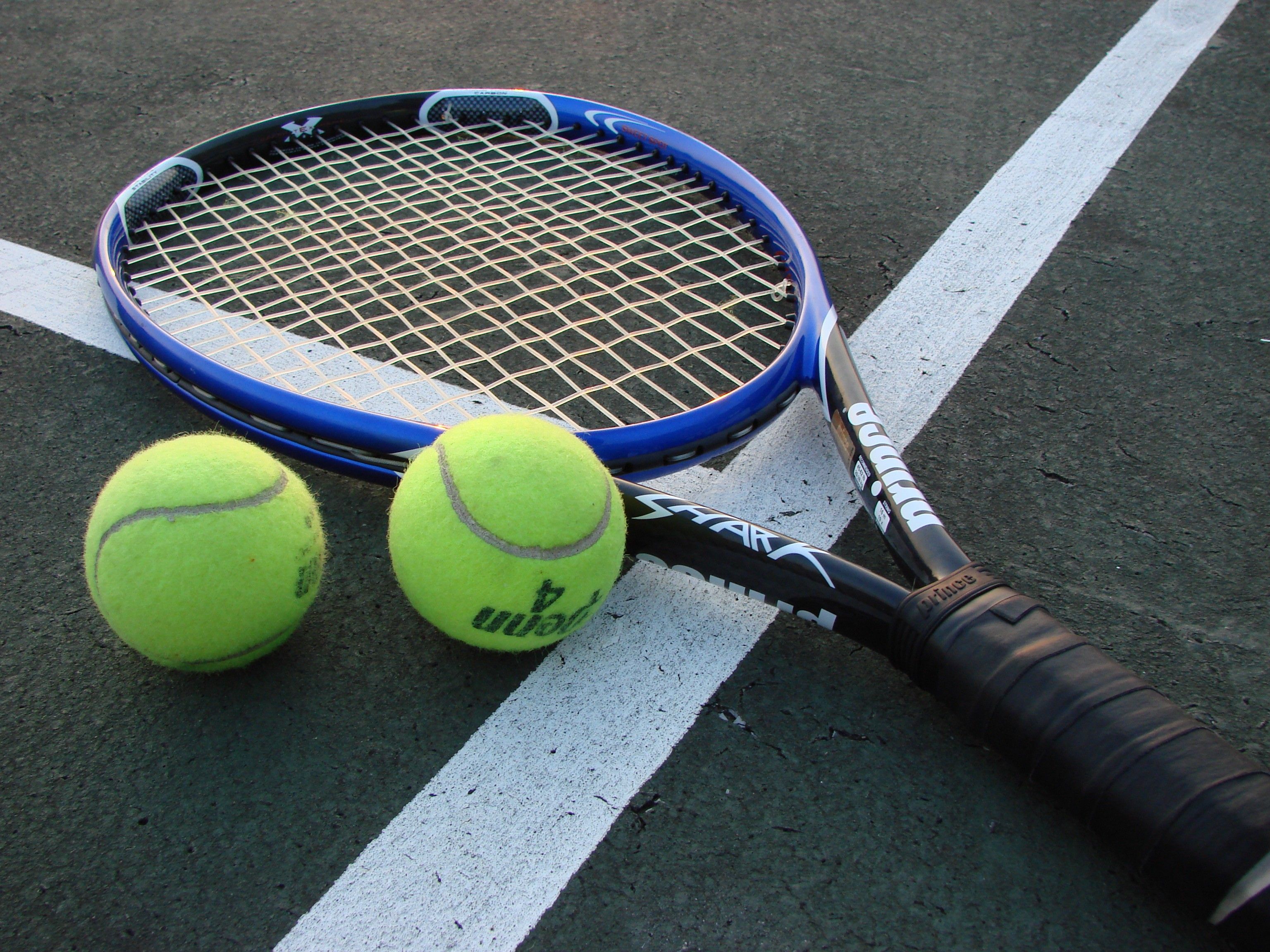 A tennis racket and two tennis balls on a tennis court. - Tennis
