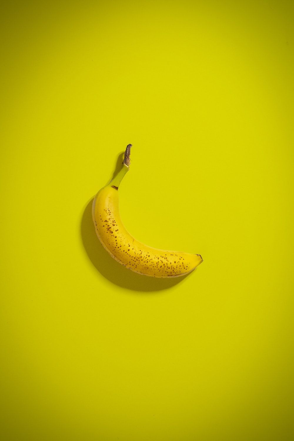 A single banana on top of yellow background - Banana