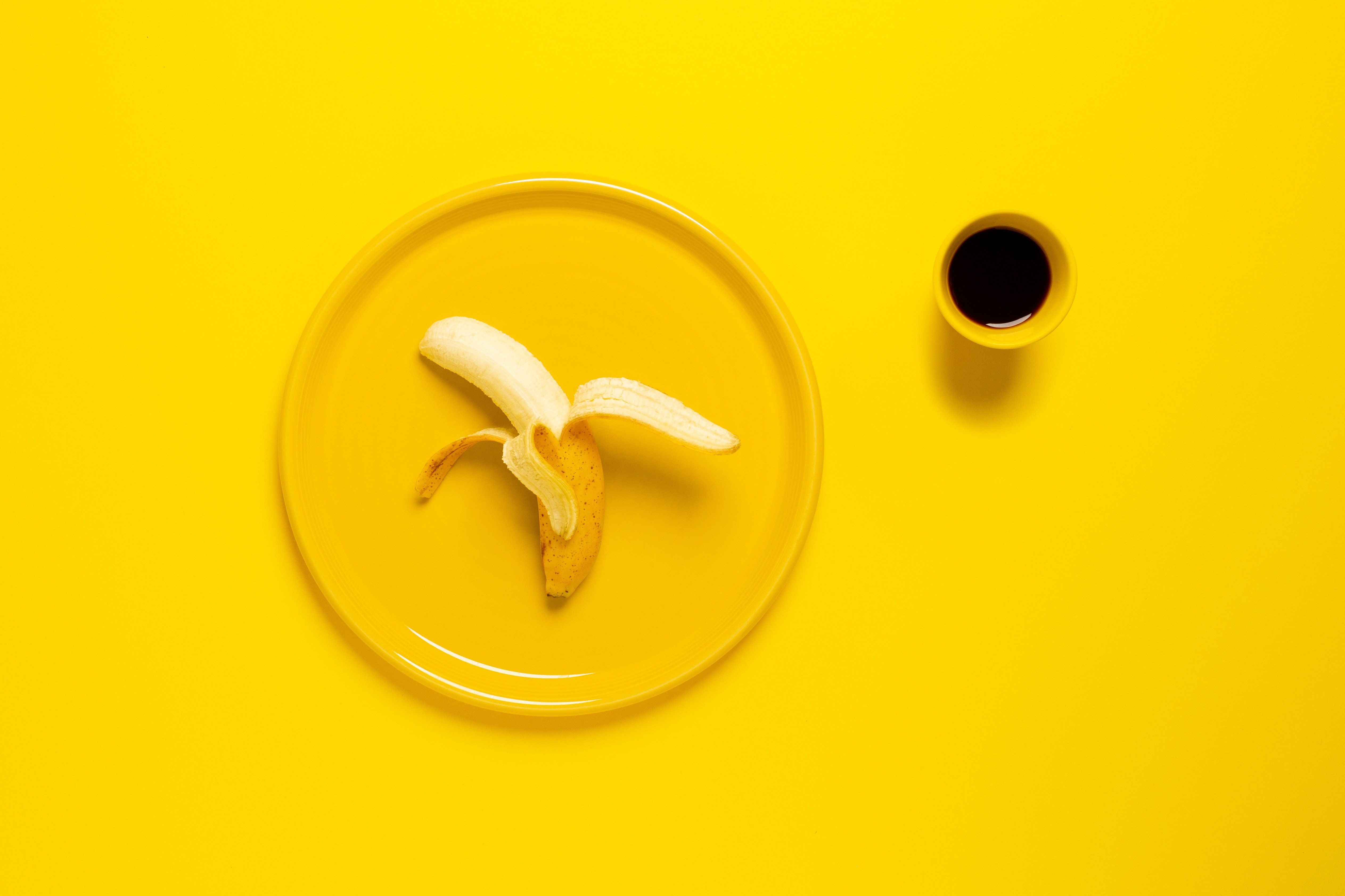 A peeled banana on a yellow plate next to a yellow cup of coffee. - Banana