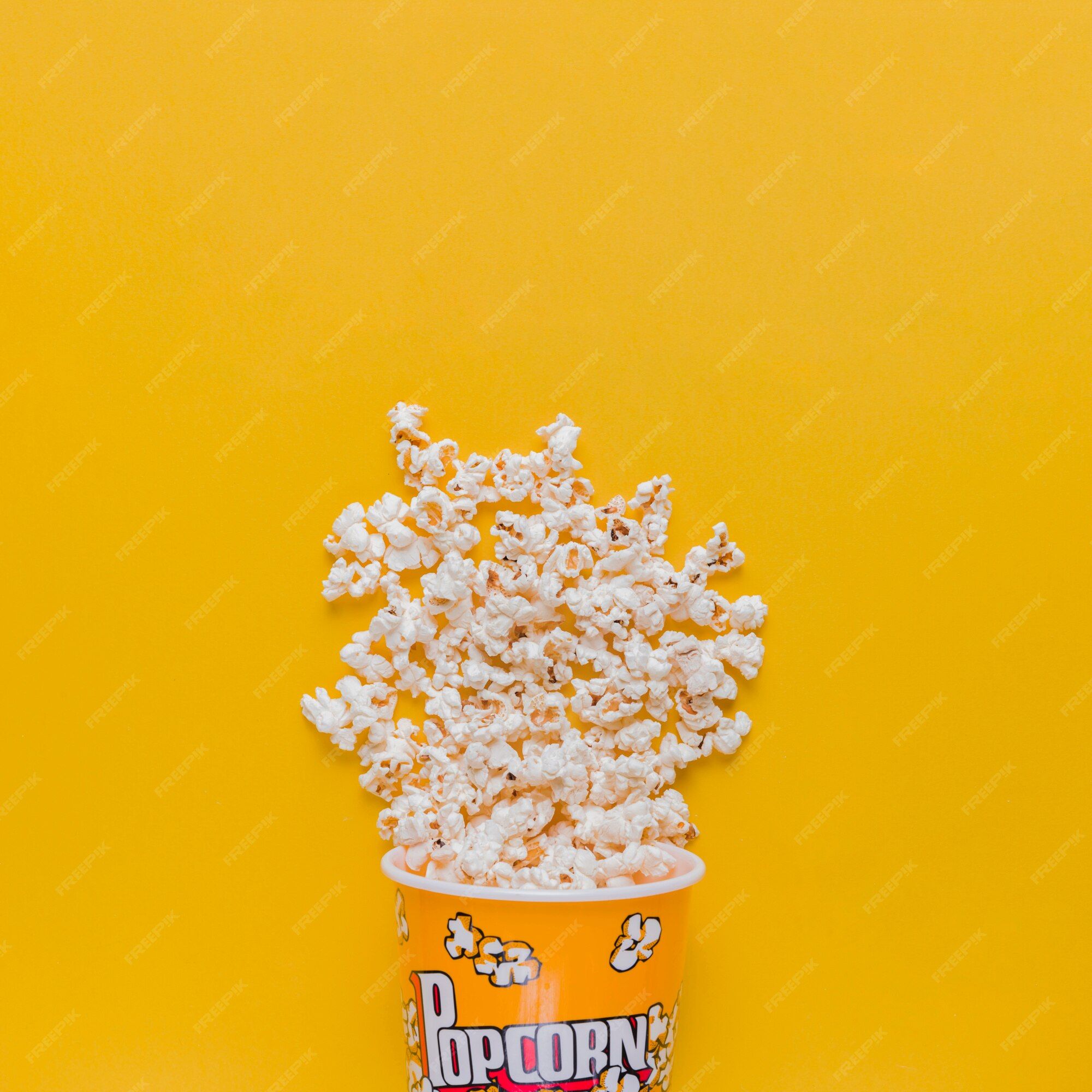 A yellow popcorn bucket with popcorn spilling out of it on a yellow background - Popcorn