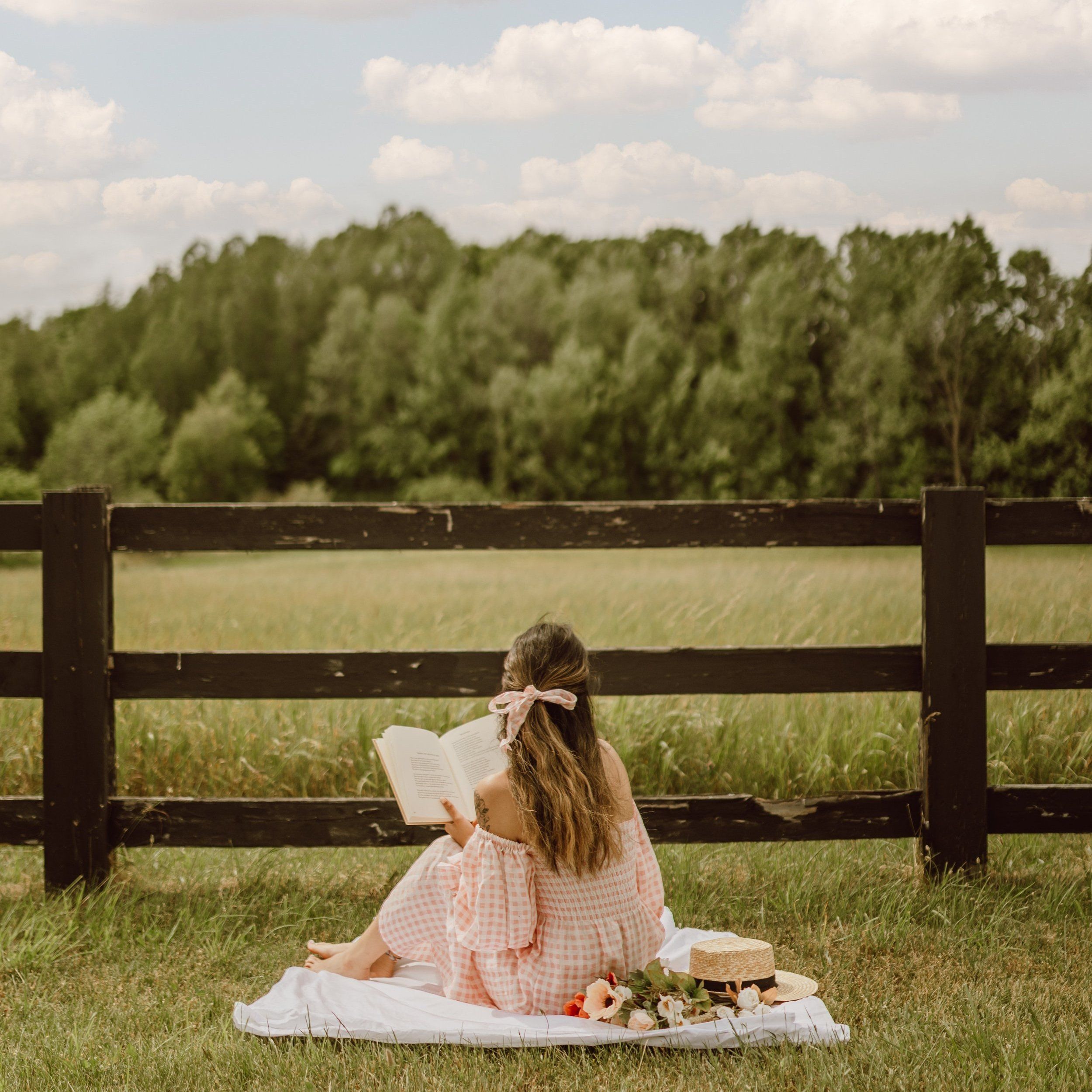 A woman sitting on a blanket in a field reading a book. - Light academia