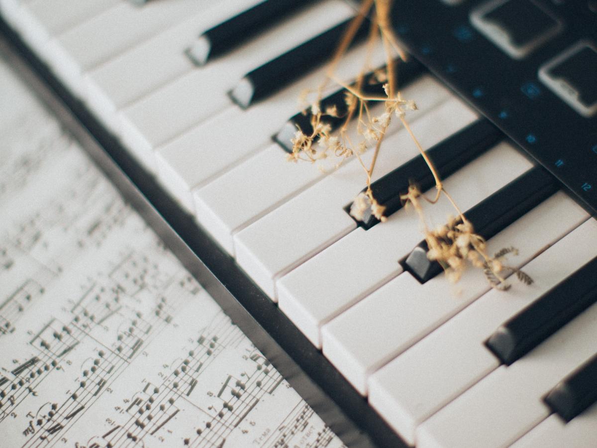 A keyboard with sheet music and a dried flower on top - Piano