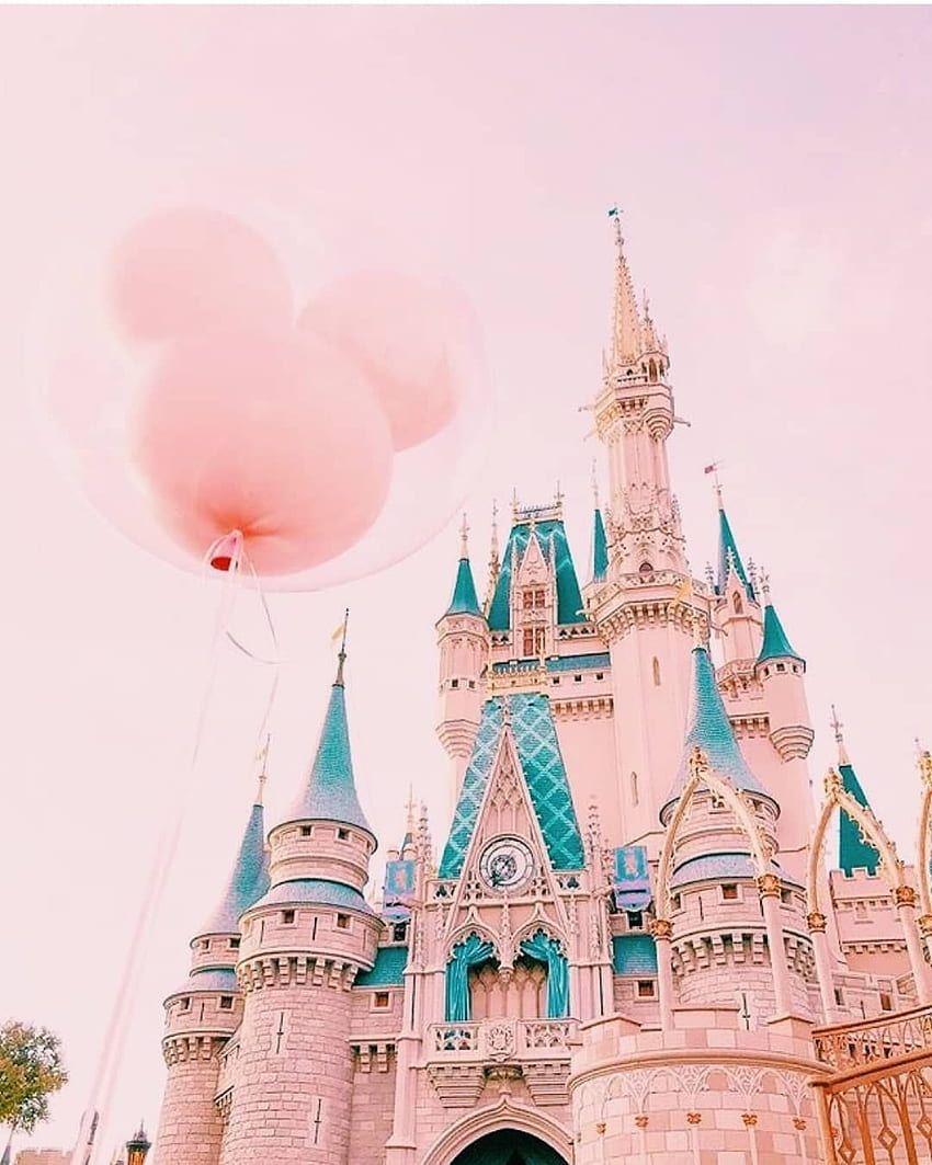 A pink balloon in the shape of a mouse is floating in front of the pink and blue Disney castle. - Disneyland