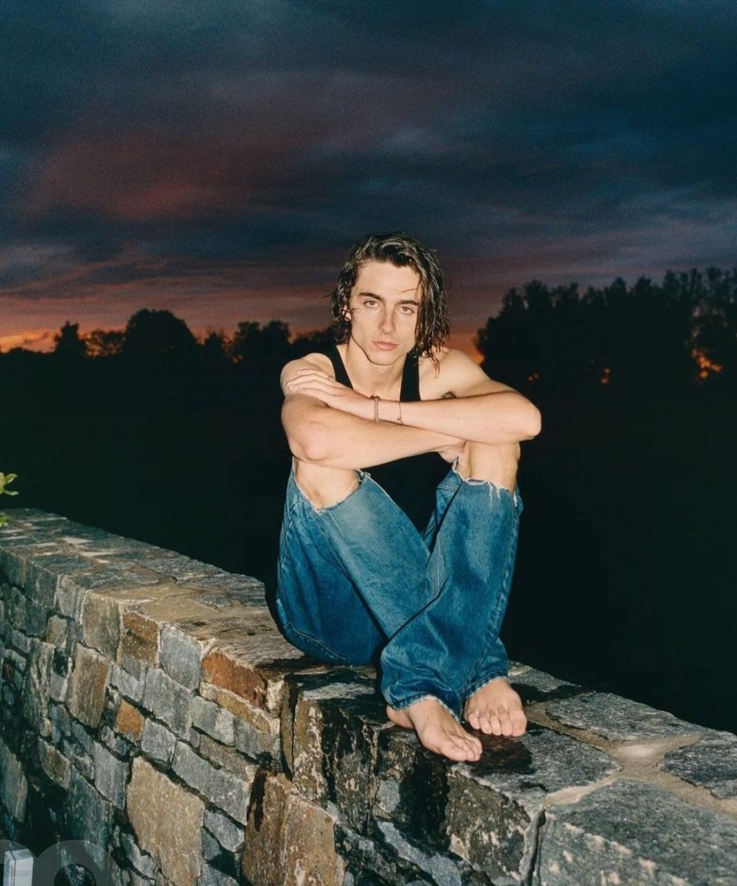 A man sitting on a brick wall with his arms crossed - Austin Abrams