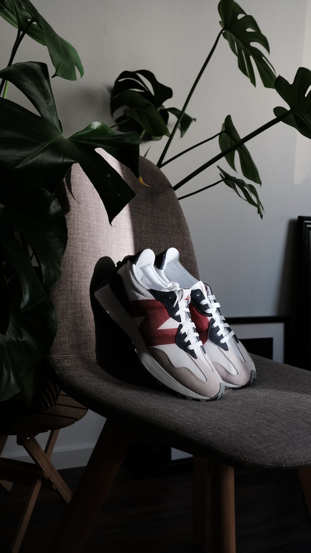A pair of sneakers sitting on a chair next to a plant. - New Balance