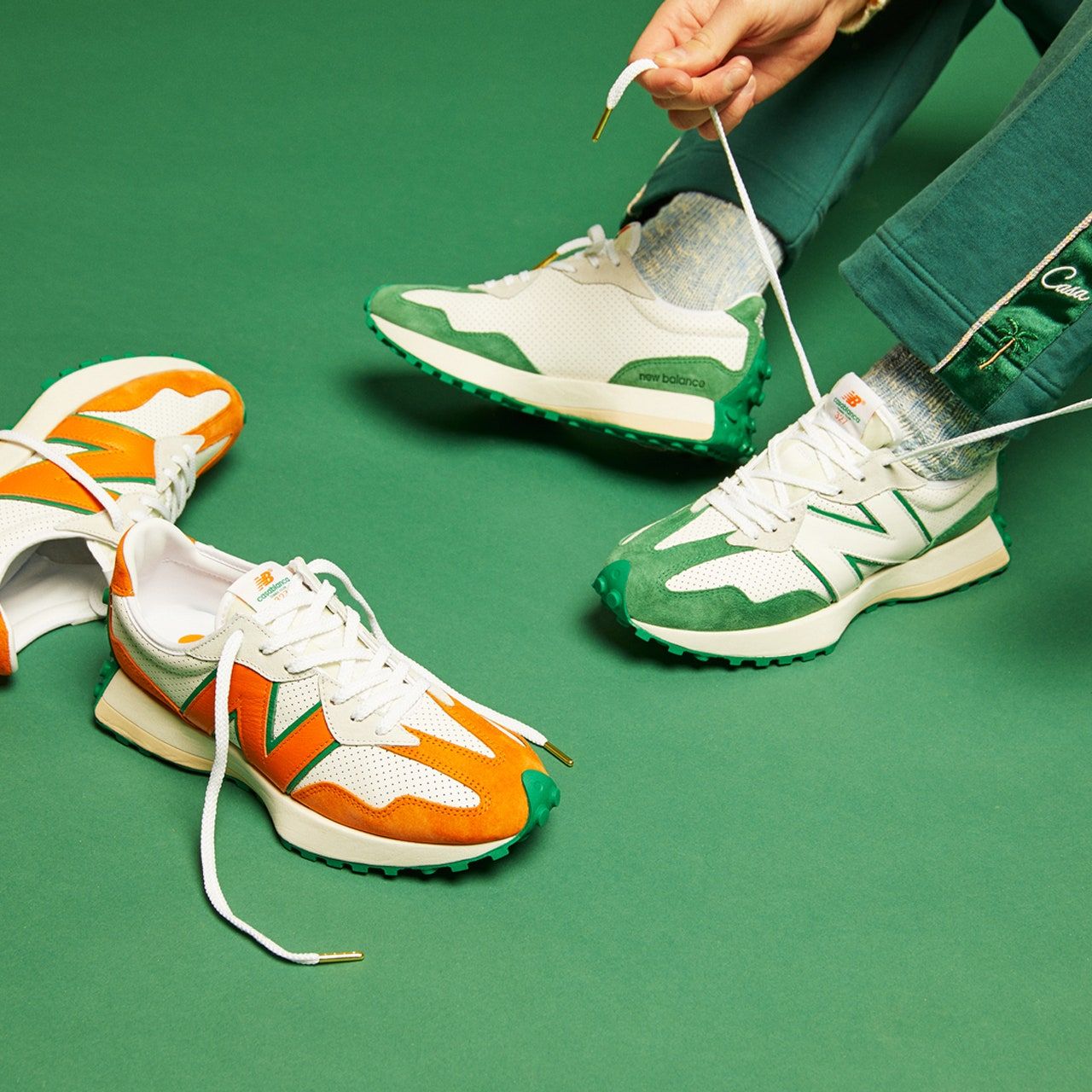 A person lacing up a pair of white, orange and green sneakers - New Balance