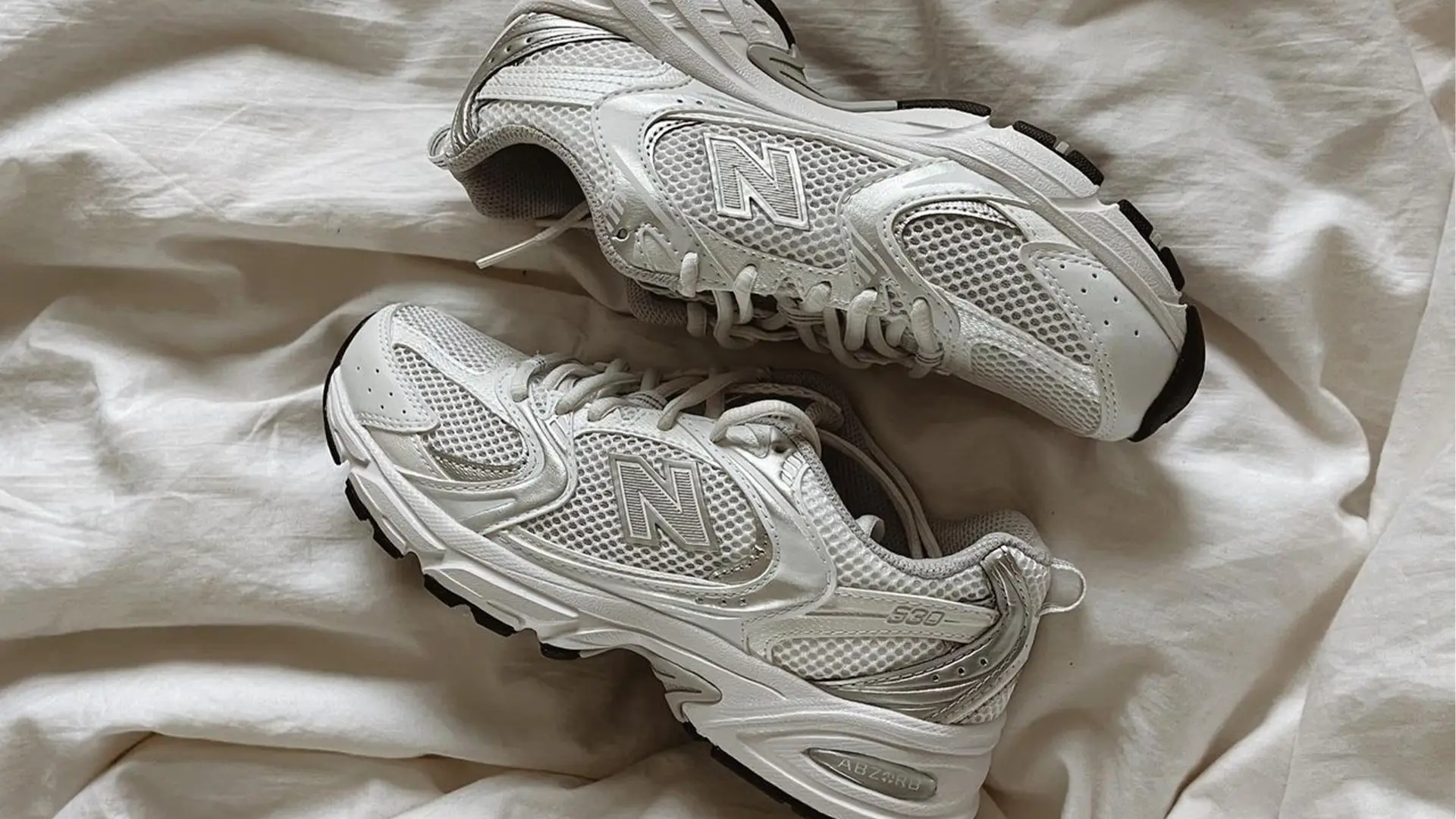 A pair of white New Balance sneakers on a white sheet. - New Balance