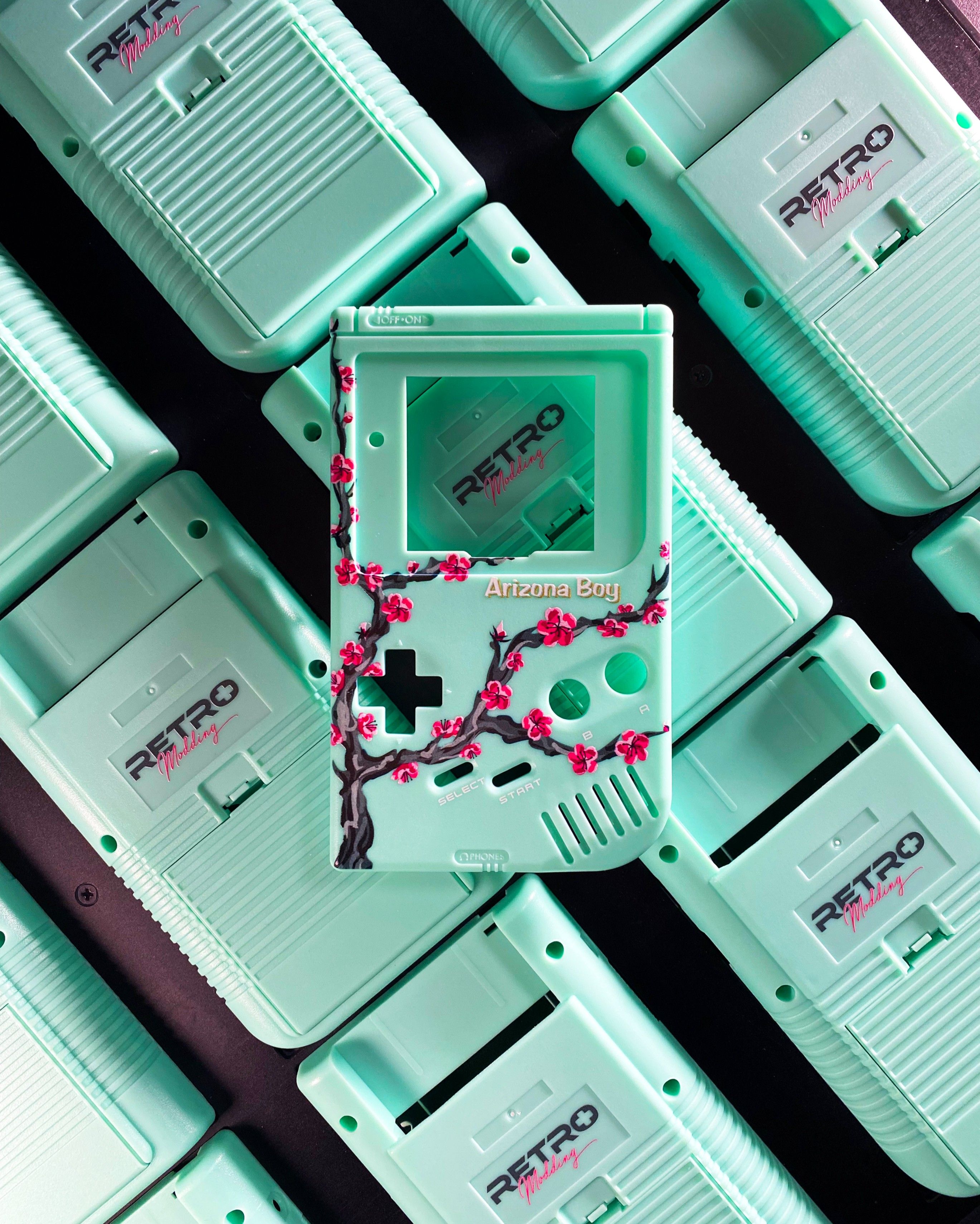 A collection of mint green Gameboy shells with one featuring cherry blossoms. - Game Boy