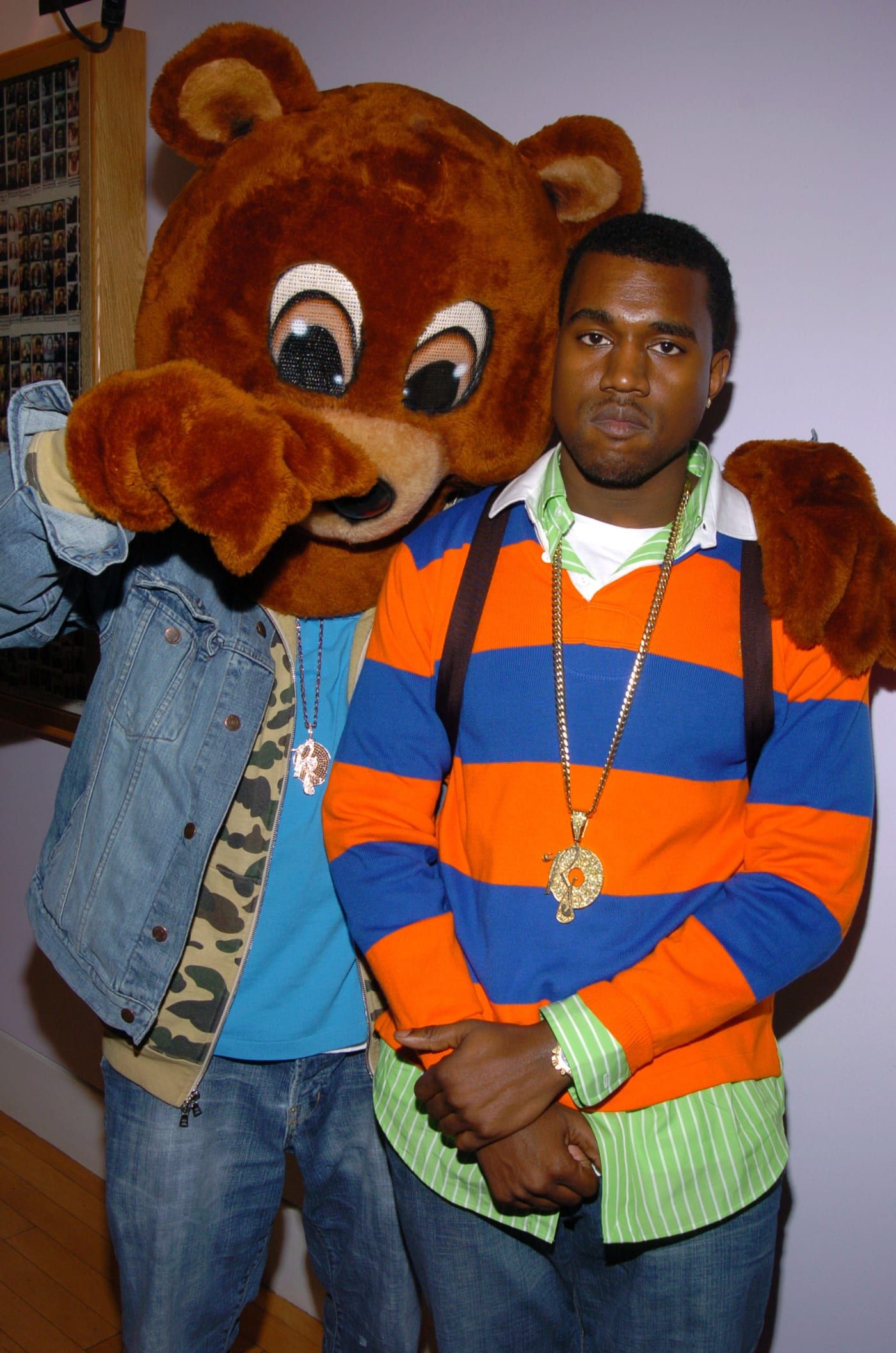 A man in an orange and blue shirt next to another person wearing bear costume - Kanye West