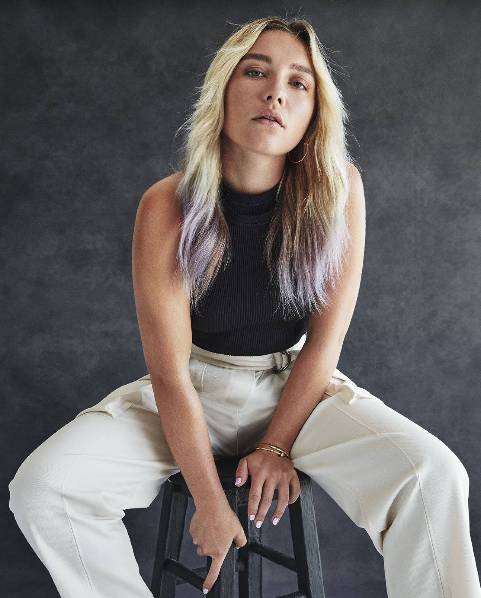 A woman with blonde hair and purple ends sits on a stool. - Florence Pugh
