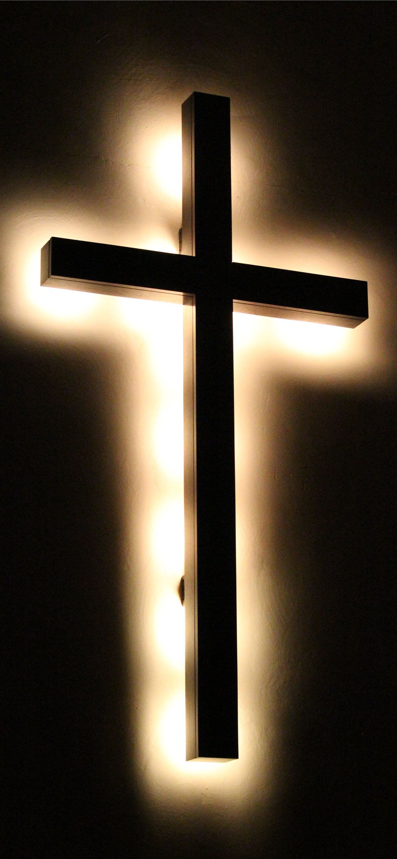A wall cross with lights shining on it. - Cross