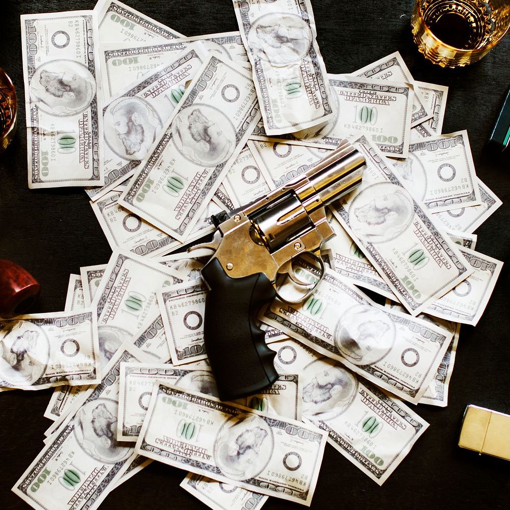 Money, a gun, and a glass of alcohol on a table. - Money