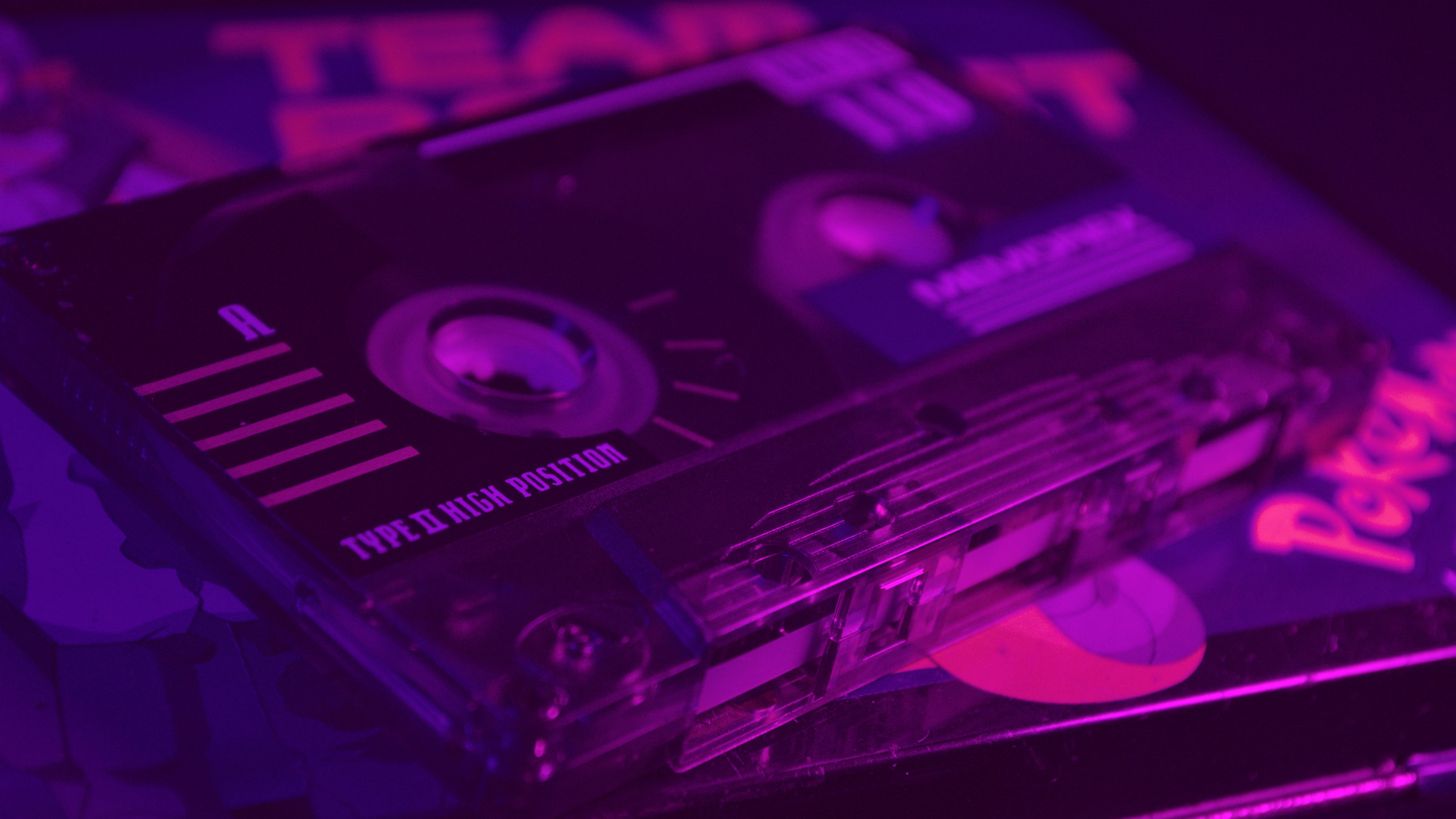 A purple and pink neon light shines on a stack of cassette tapes. - Bisexual