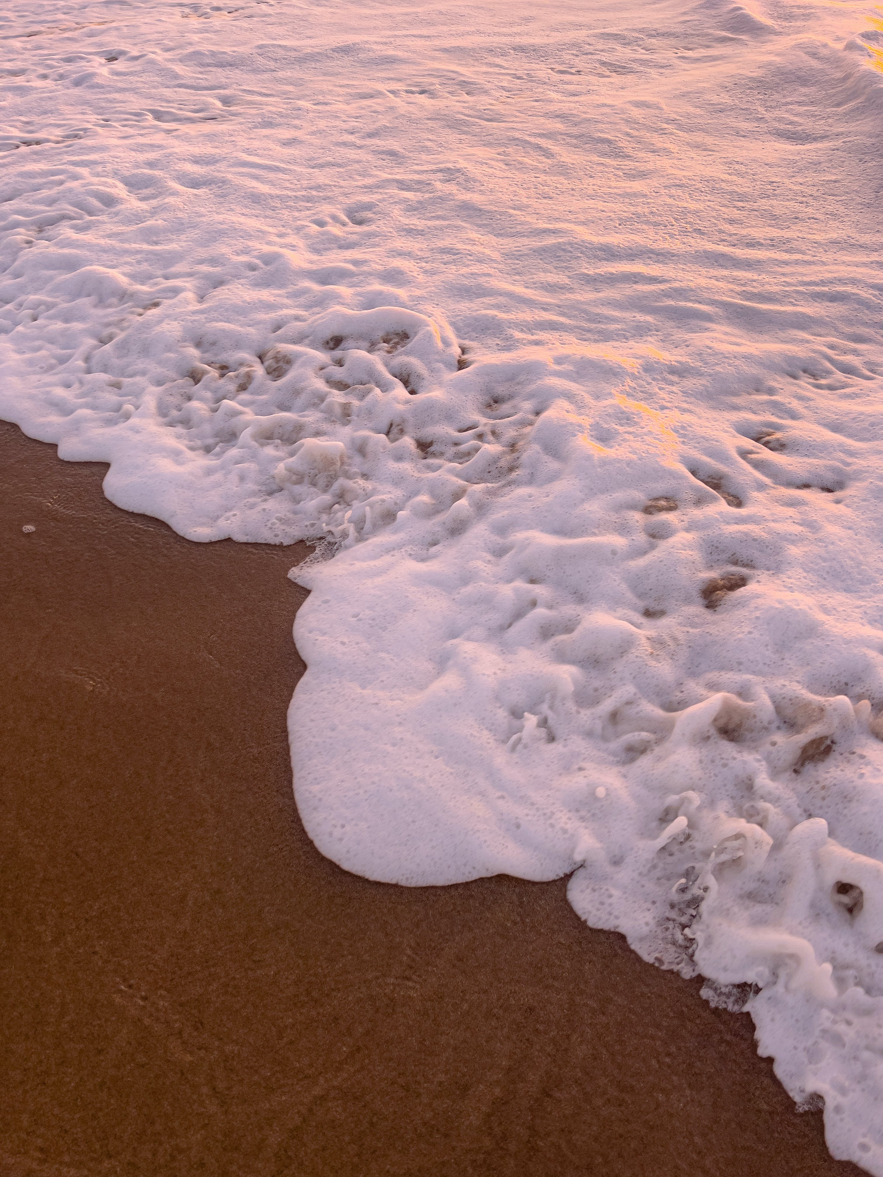 A beach with waves and sand at sunset