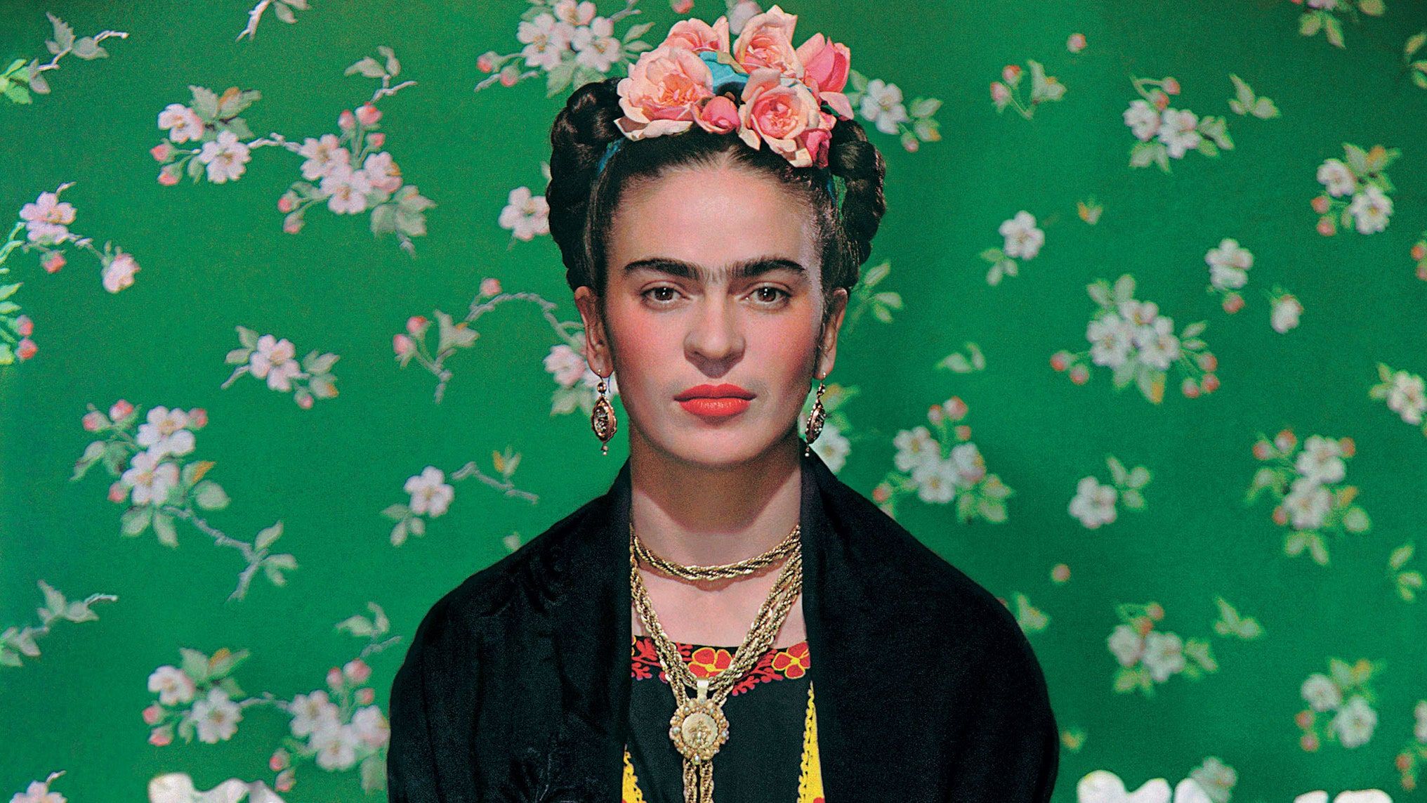 Frida Kahlo in front of a green background with flowers. - Frida Kahlo