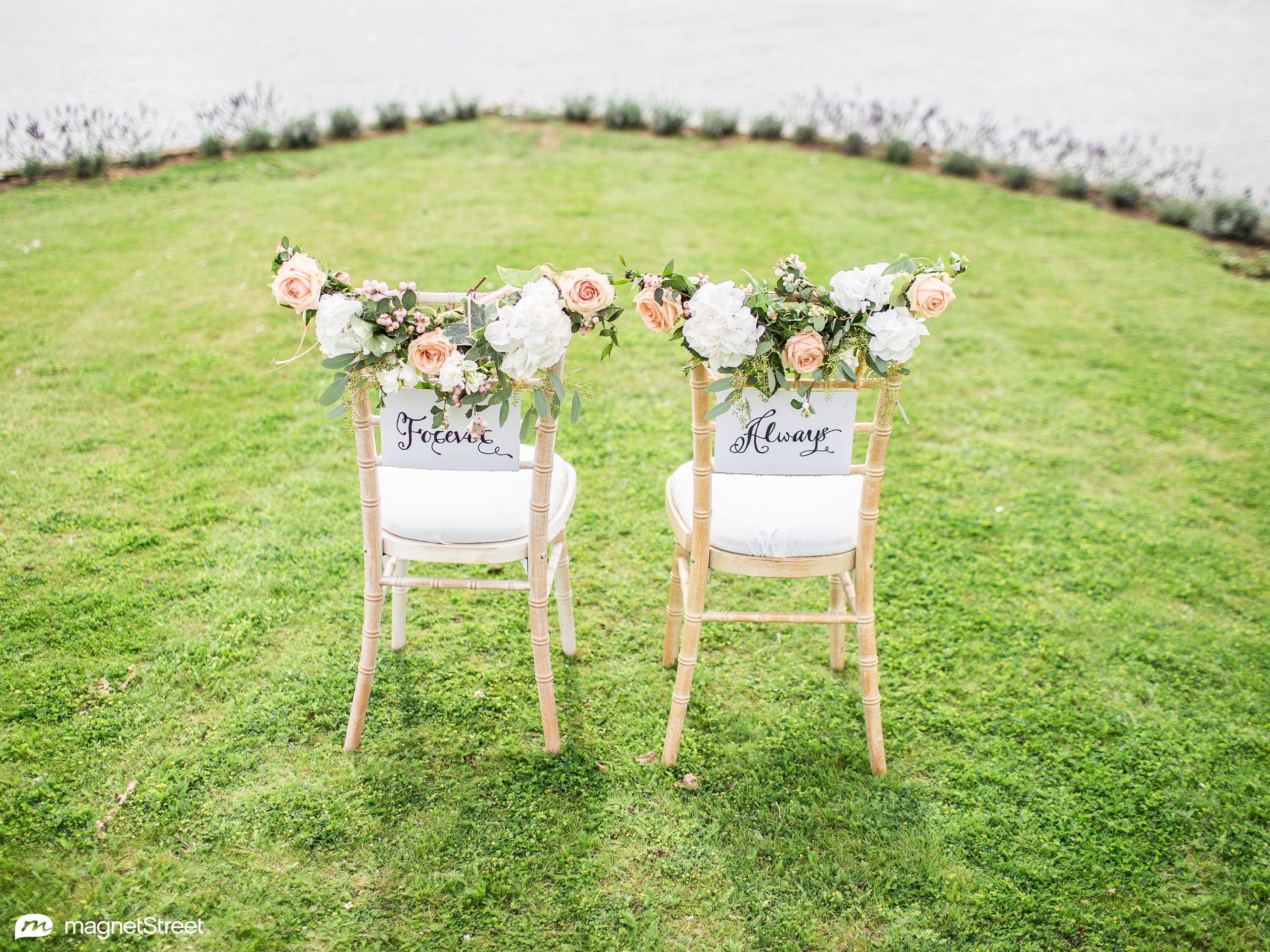 Two chairs with flowers on them sitting next to a lake - Wedding