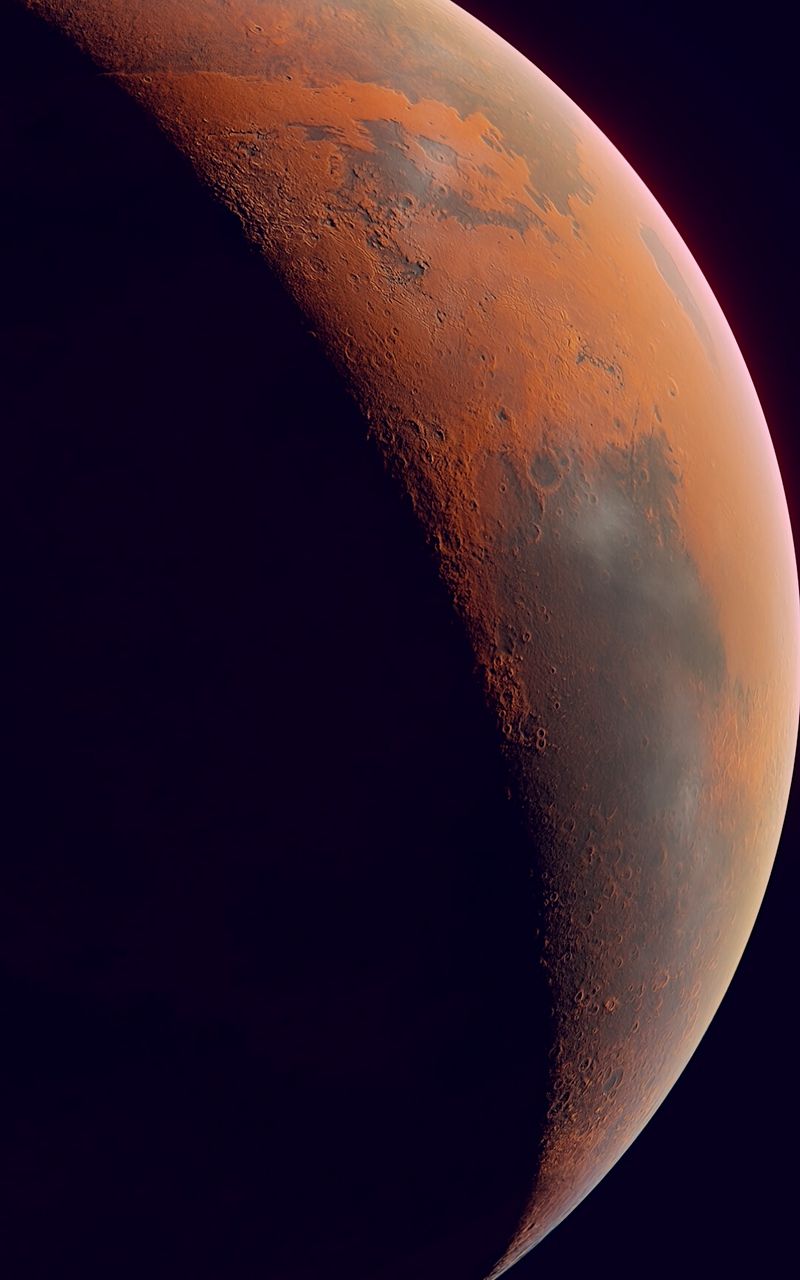 The planet Mars, with its reddish-brown surface and dark side. - Mars