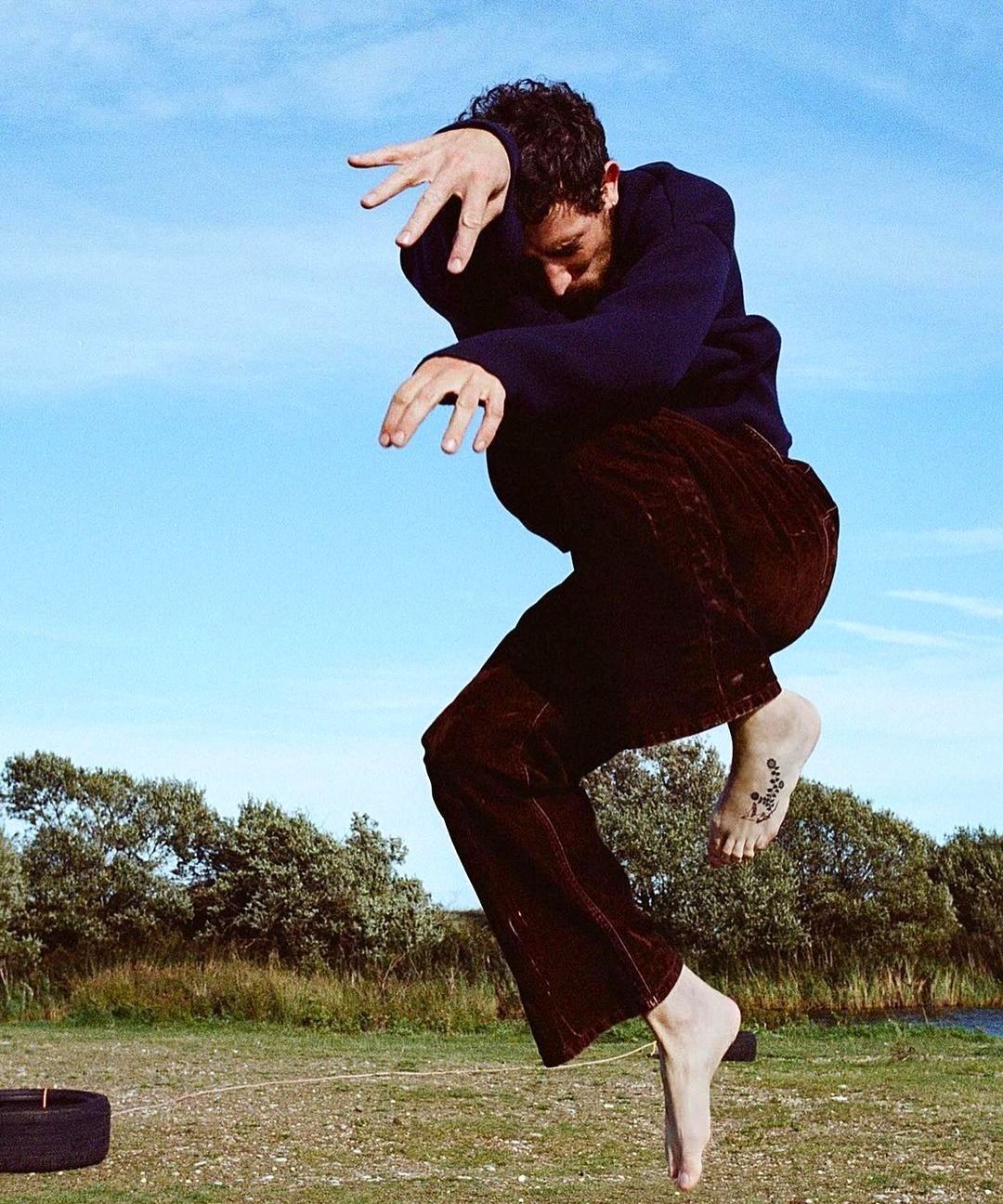 A man in a black shirt and brown pants jumping in the air - Josh O'Connor