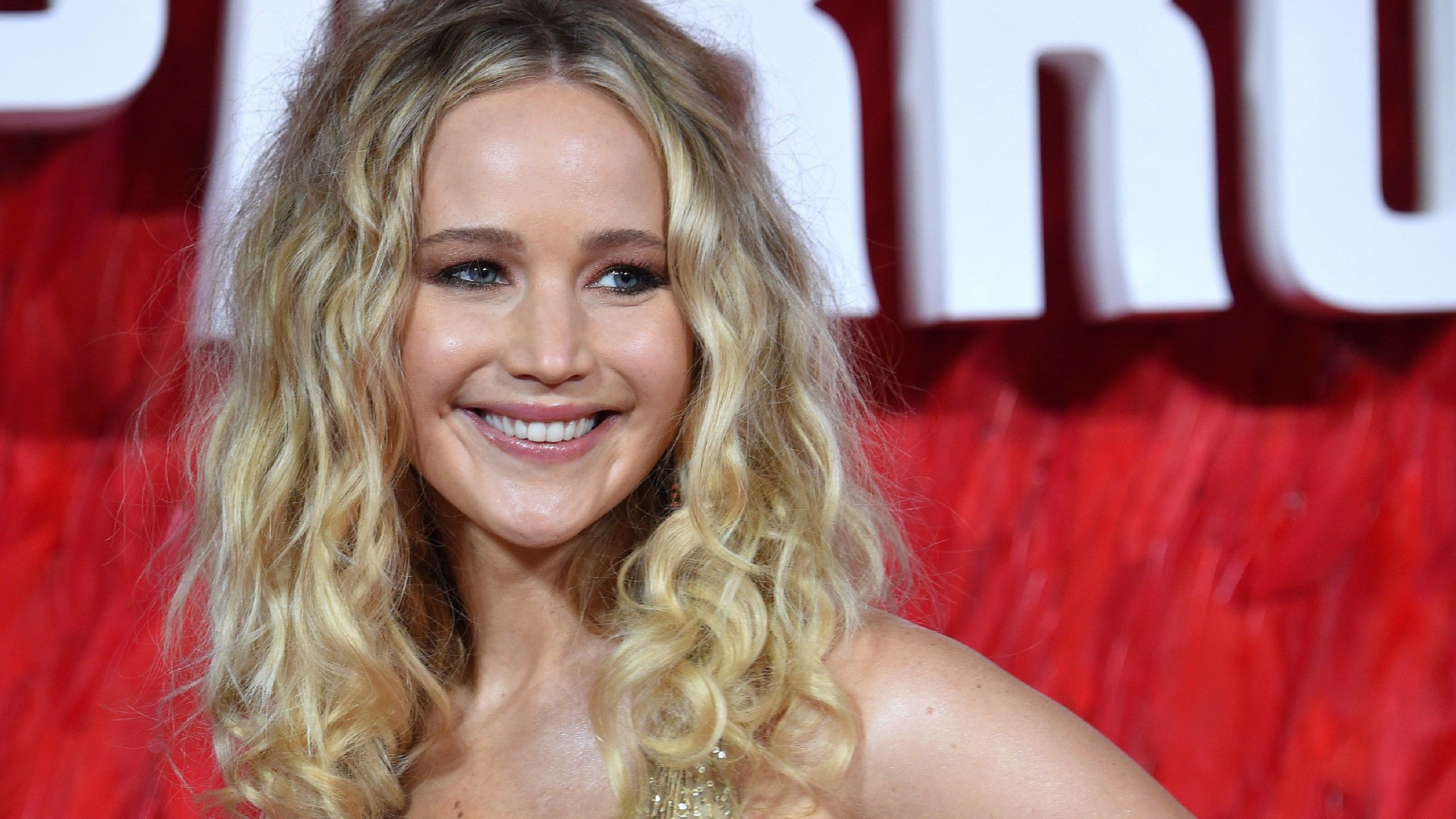 Jennifer Lawrence smiling on a red carpet in a gold dress - Jennifer Lawrence