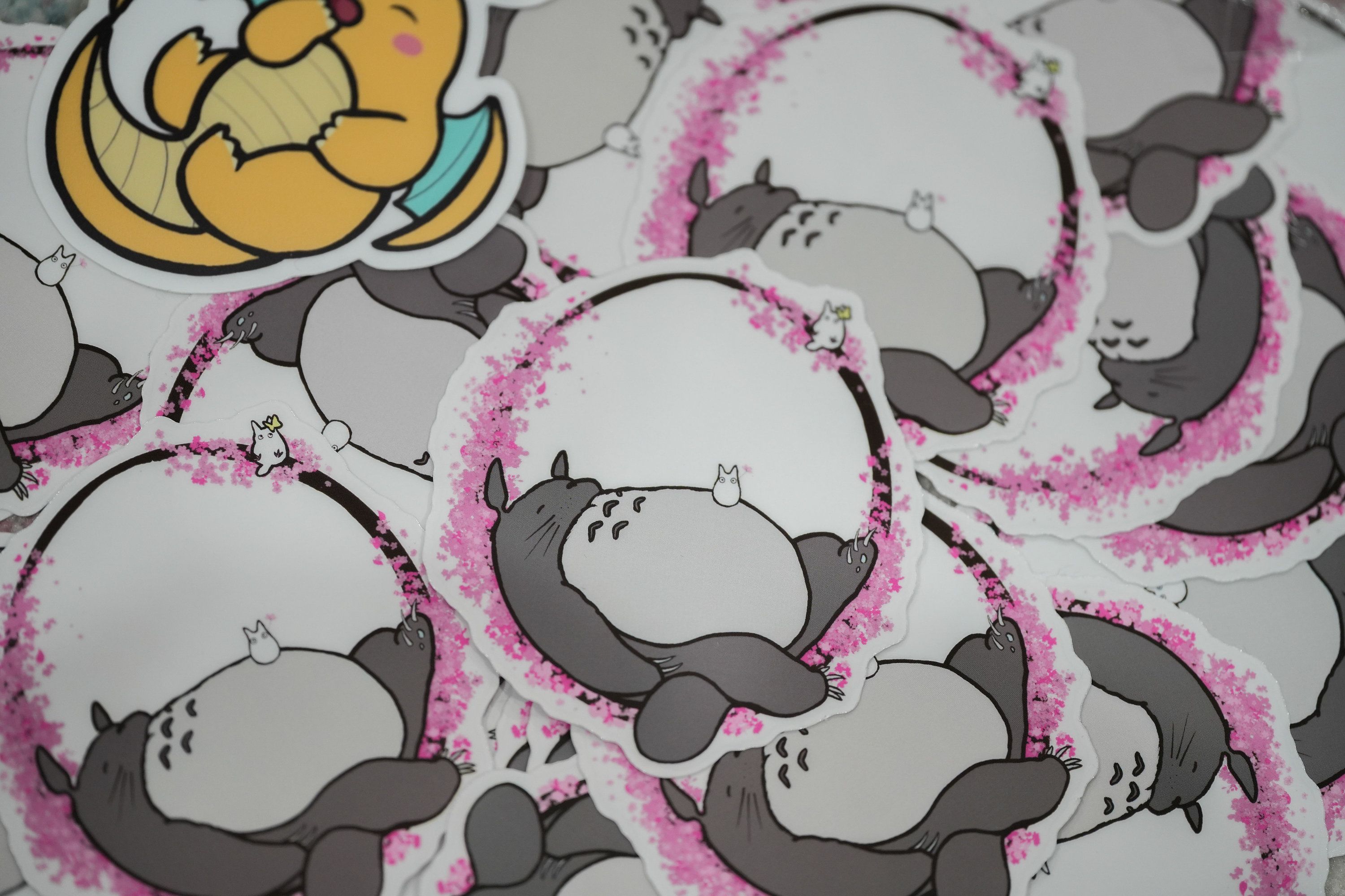 A pile of round stickers with a black cat sleeping on a pile of pink flowers - My Neighbor Totoro