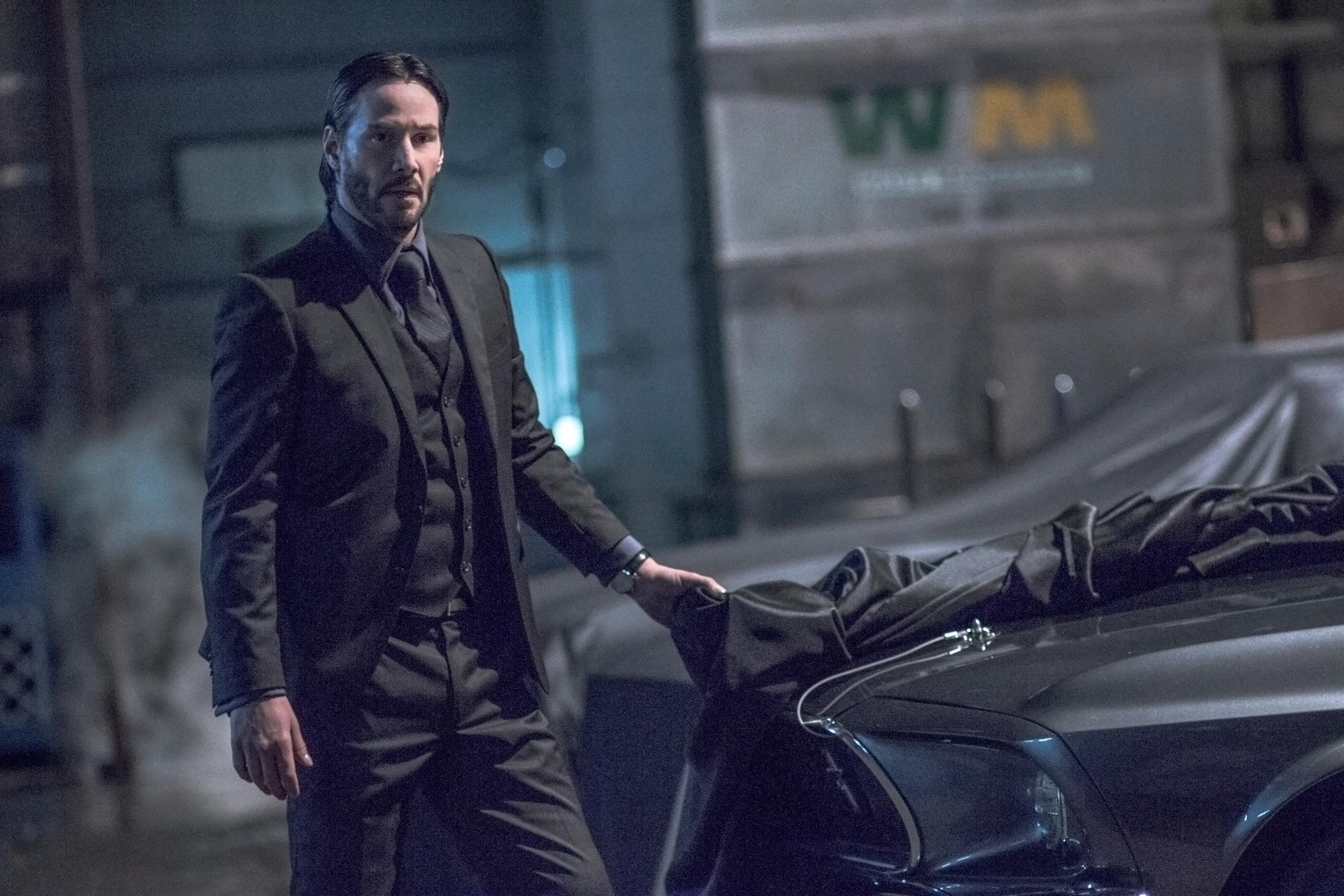 John Wick standing next to a car in a suit - John Wick