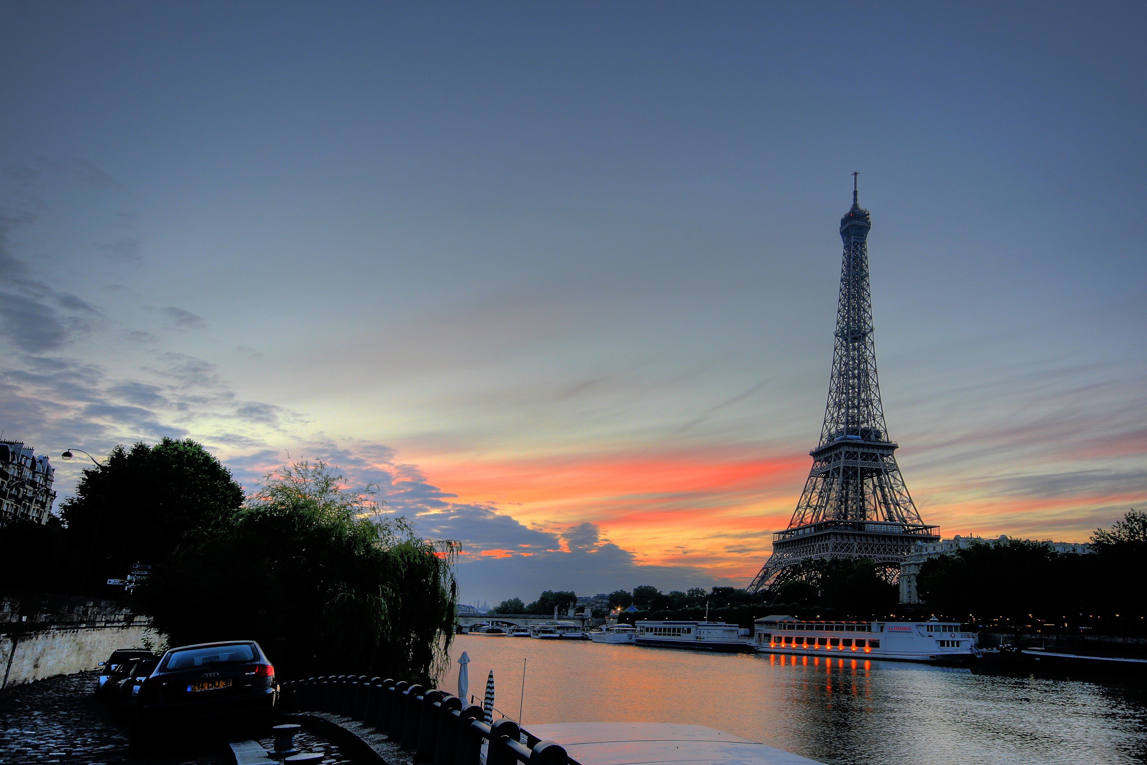 A car is parked next to a river with the Eiffel Tower in the background. - France