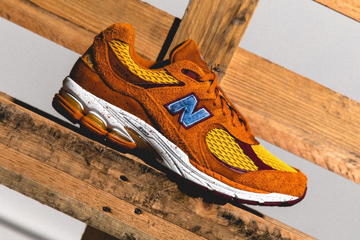 A pair of orange and yellow New Balance sneakers on a wooden plank - New Balance