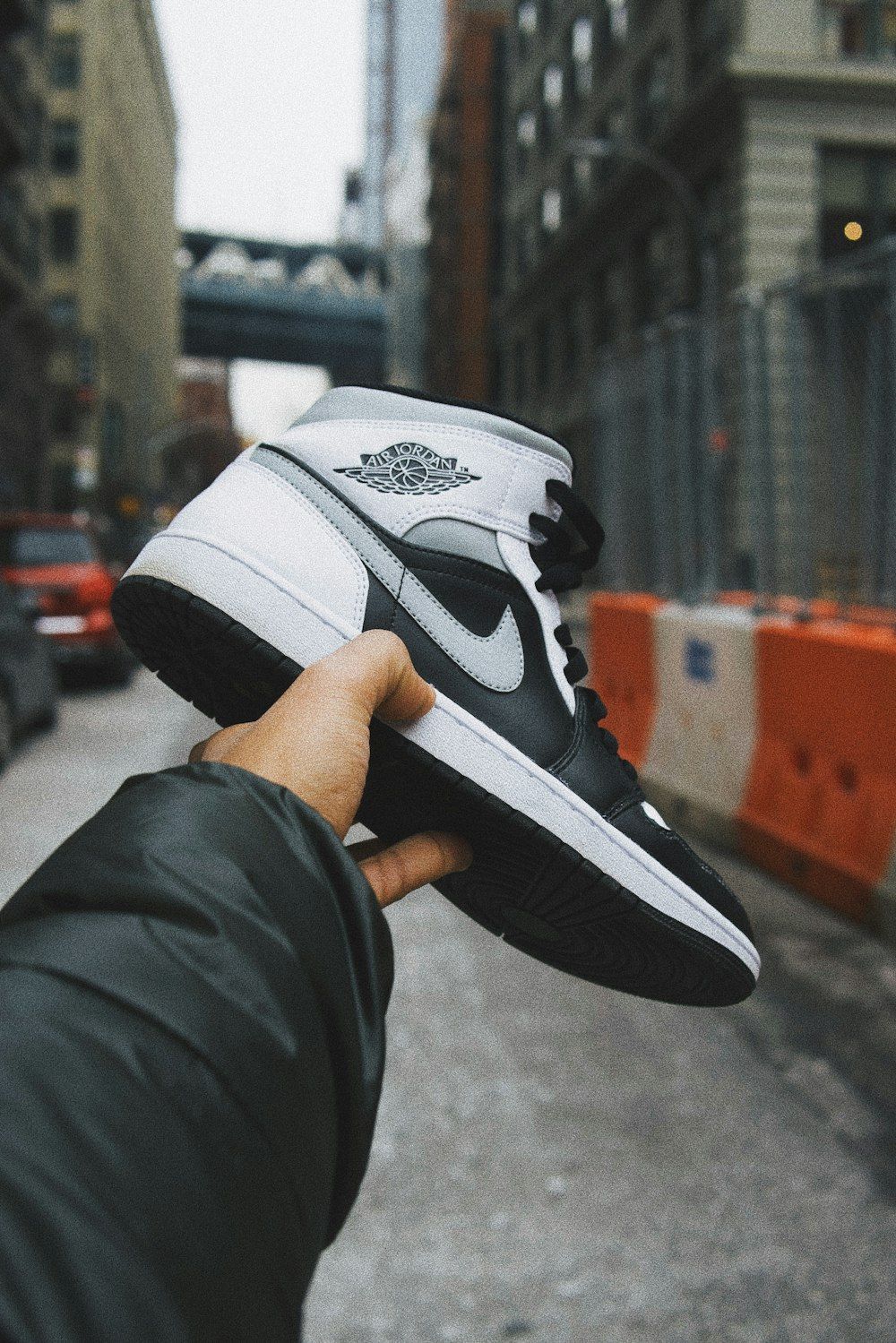 A person holding a pair of black and white Nike Jordan 1 mid in the street - Air Jordan