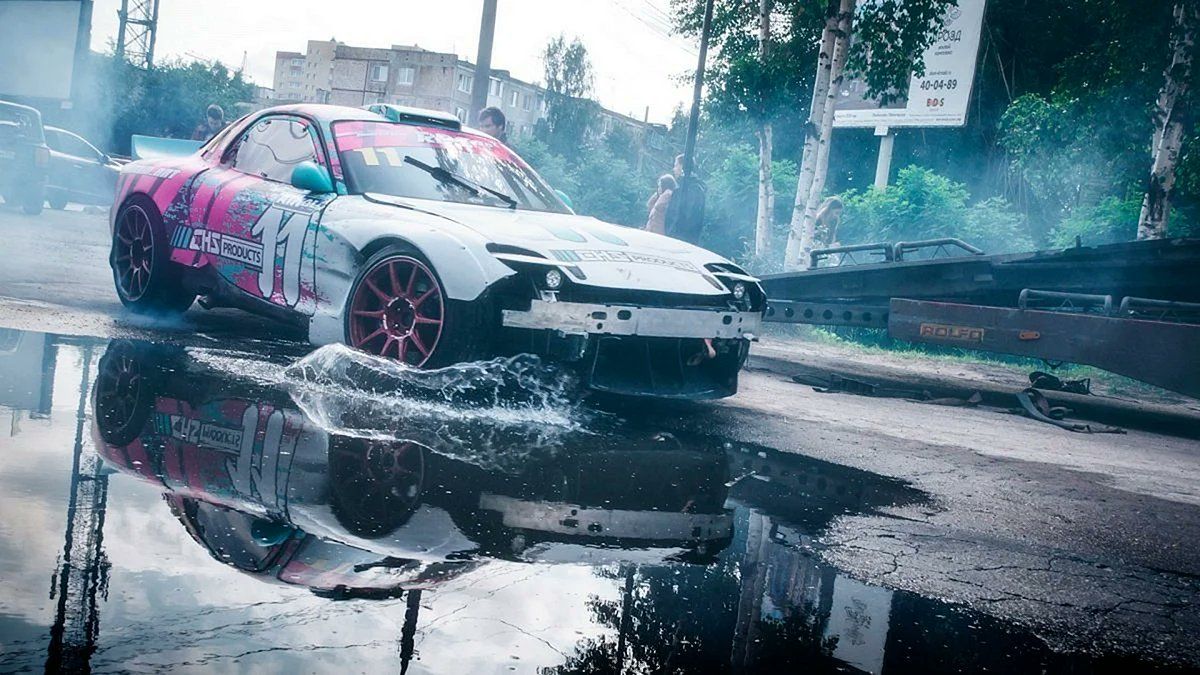 A car with a pink and white livery is drifting on a wet road - JDM