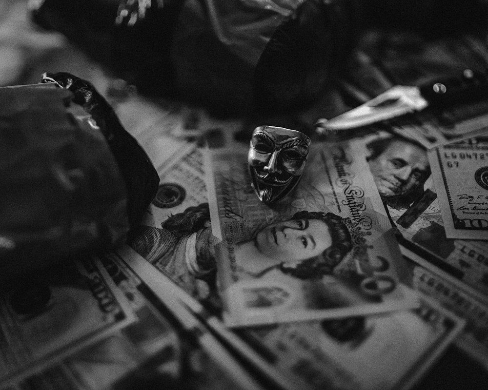 A black and white photo of a bag of money and a mask - Money