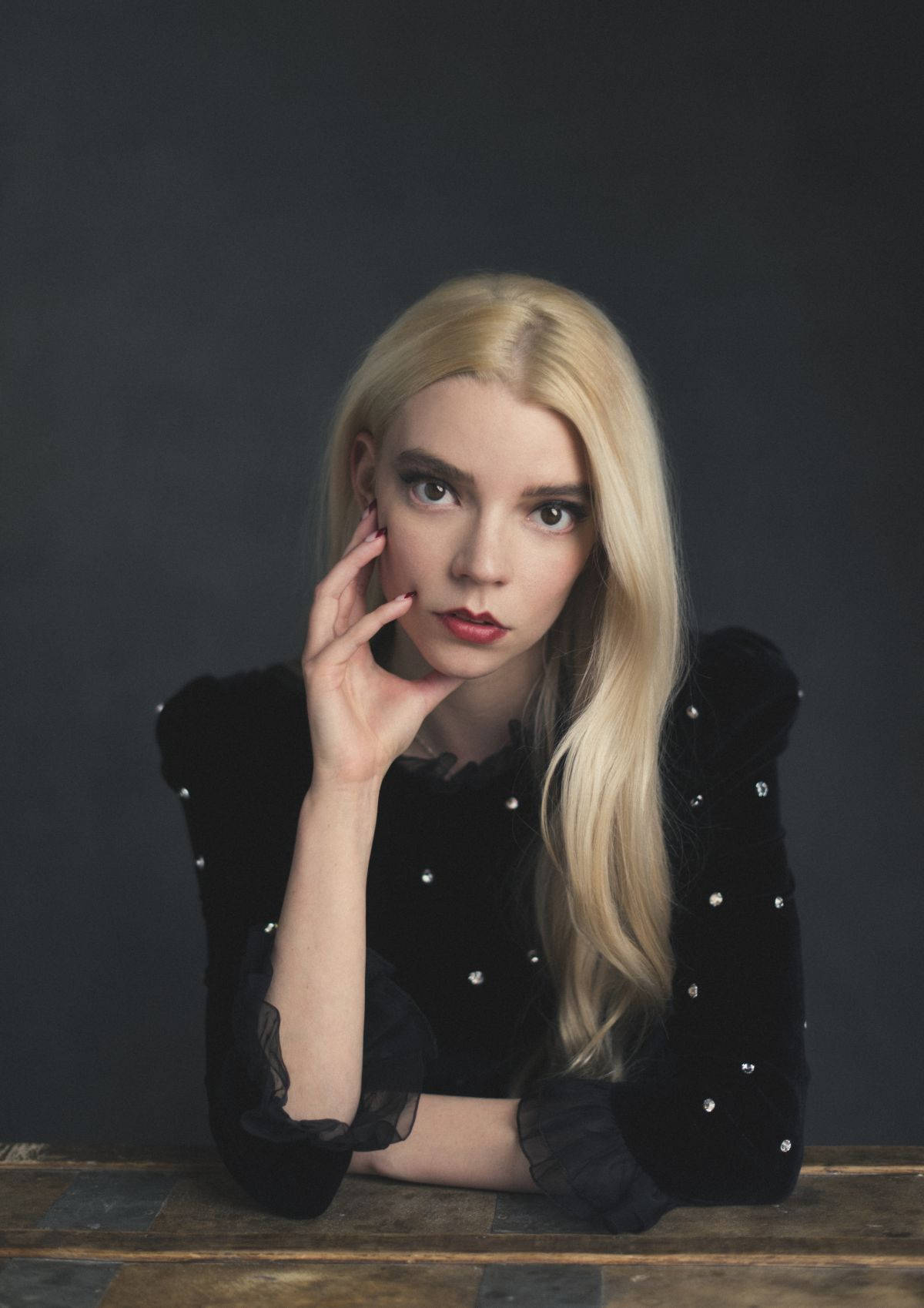 A blonde woman in a black top sits at a wooden table. - Anya Taylor-Joy