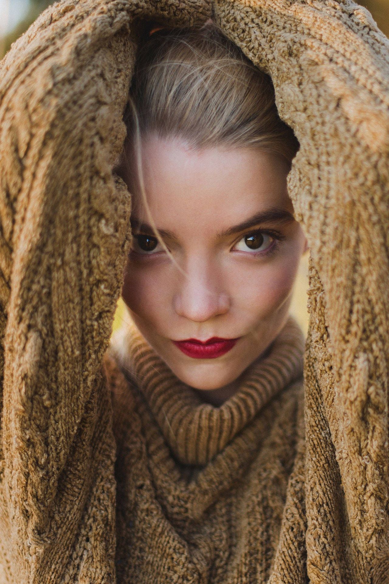 A woman with red lipstick and a tan sweater. - Anya Taylor-Joy