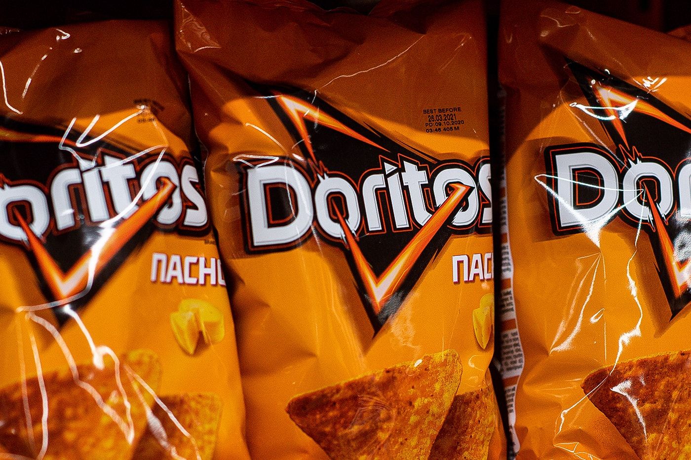 A row of bags of Doritos Nacho Cheese flavored chips. - Doritos