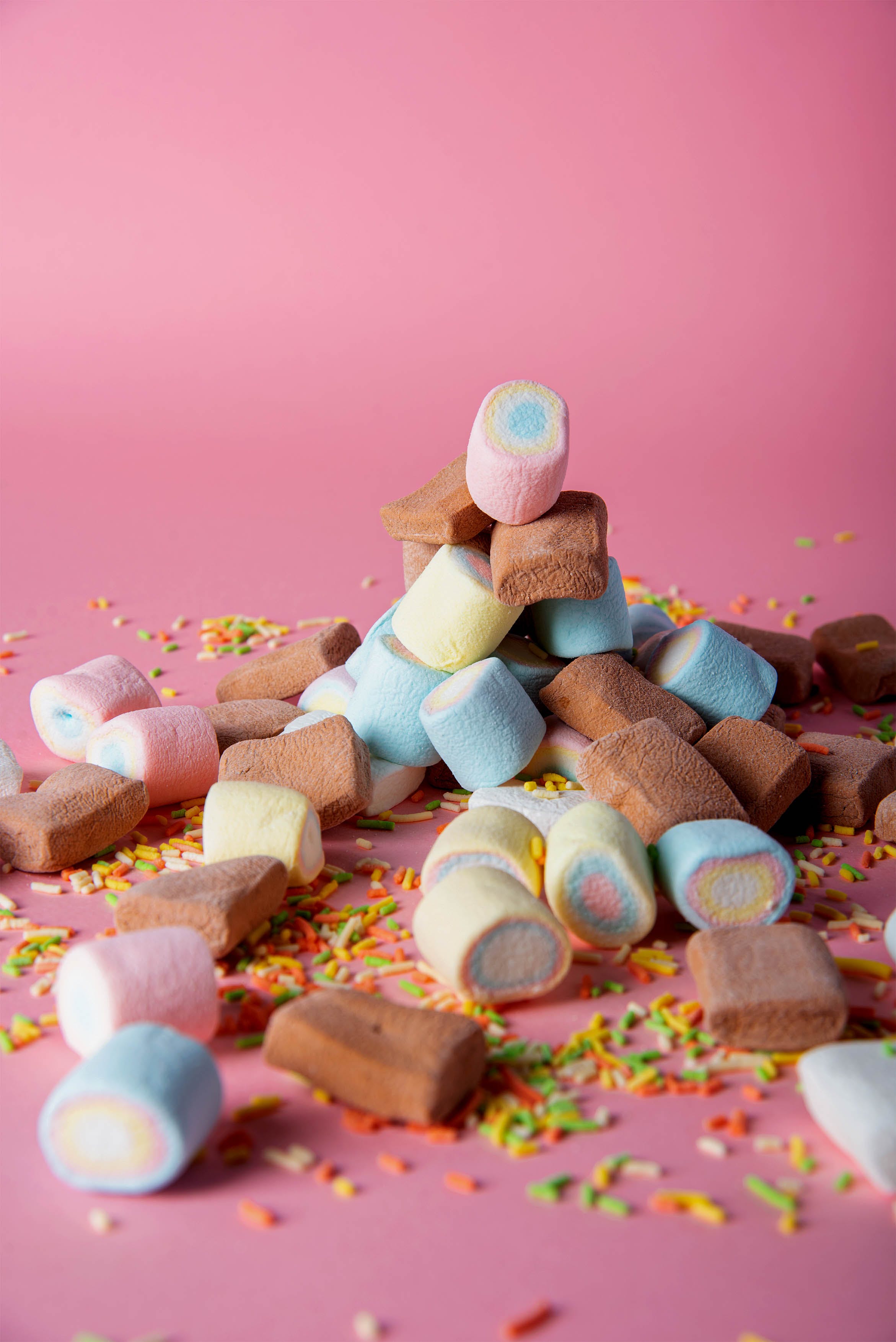 A pile of different colored marshmallows with sprinkles on a pink background - Marshmallows