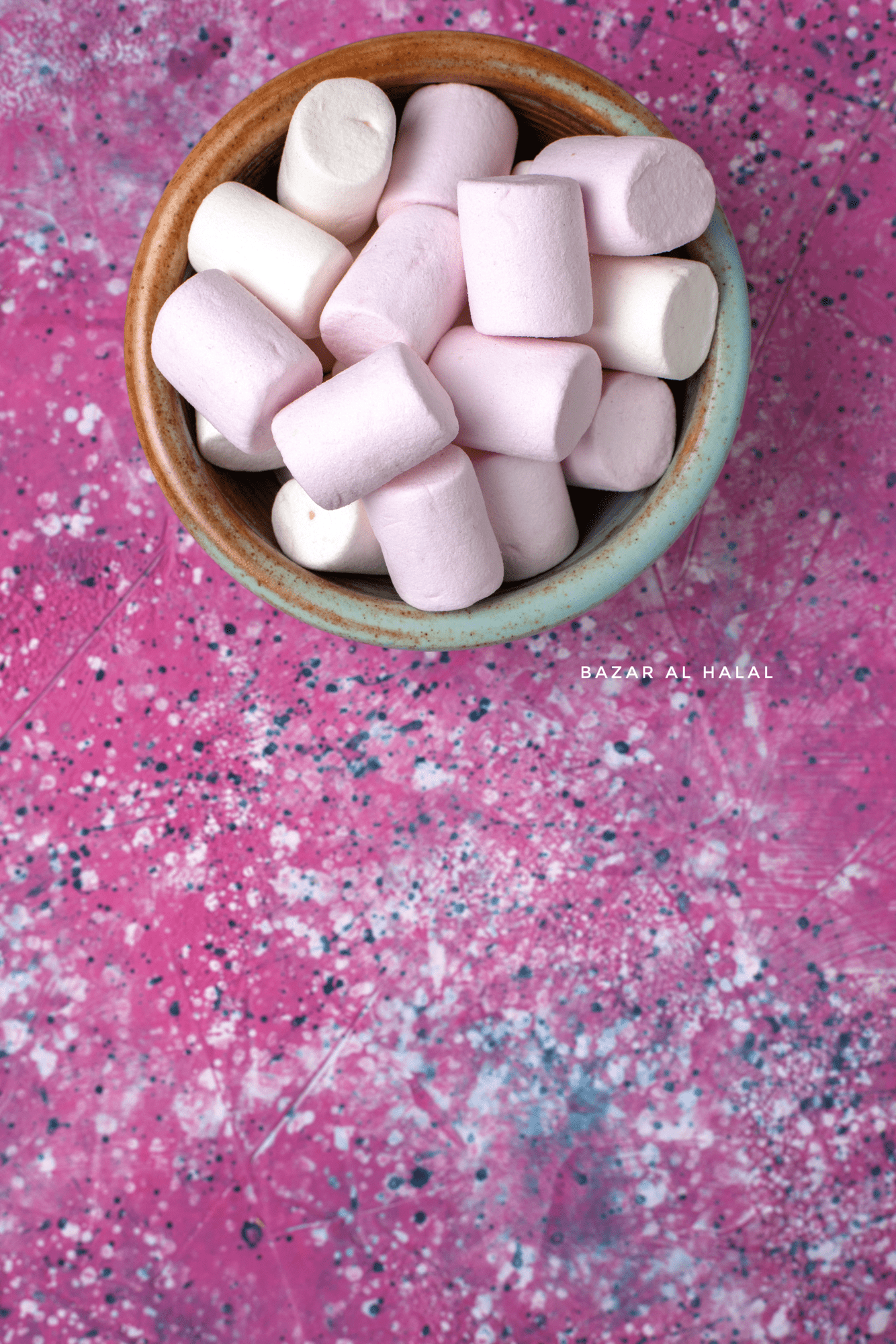 A bowl of pink and white marshmallows on a pink and purple speckled surface. - Marshmallows
