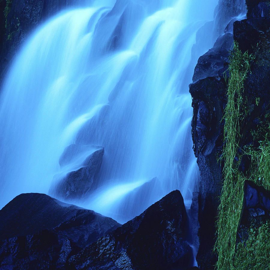 A waterfall with a blue hue cascades over rocks. - Waterfall