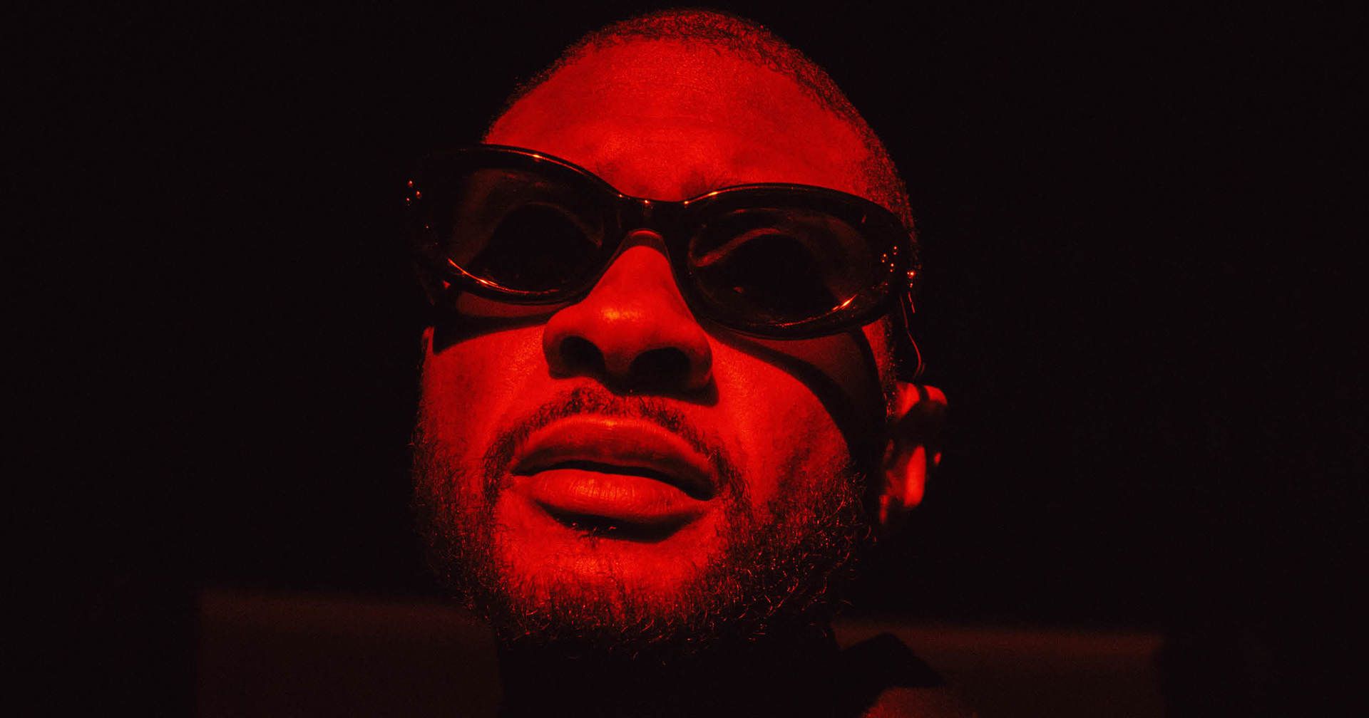 A man wearing sunglasses with a red light shining on him - Usher