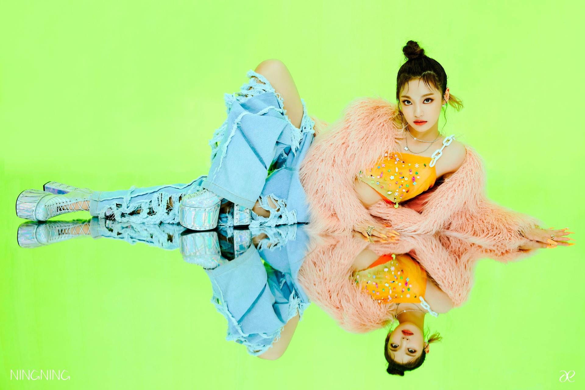 A picture of Nancy of Momoland laying on the ground with her legs crossed and wearing a blue fluffy jacket with a pink bag. - Aespa