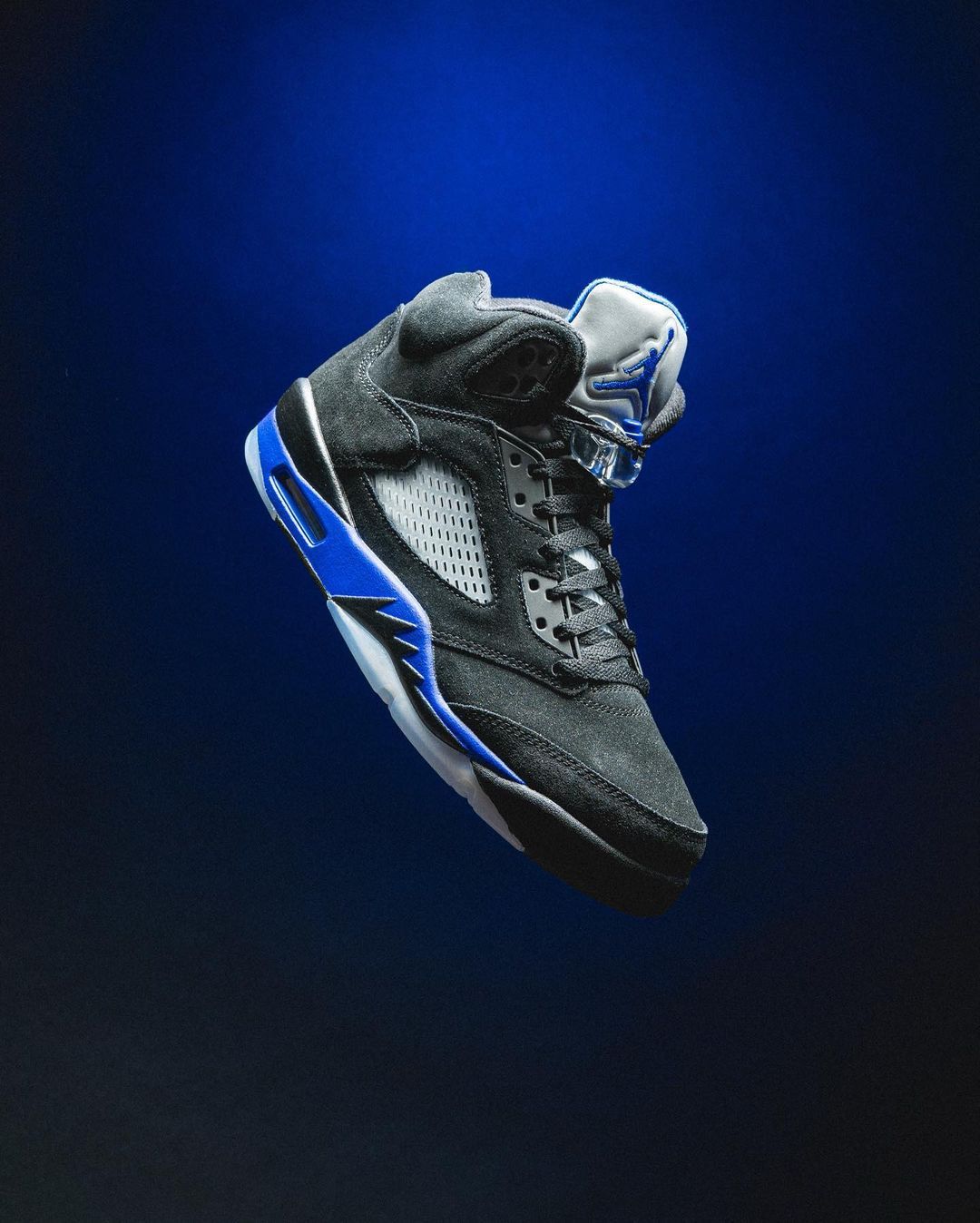 A pair of black and blue sneakers floating in the air. - Air Jordan 5