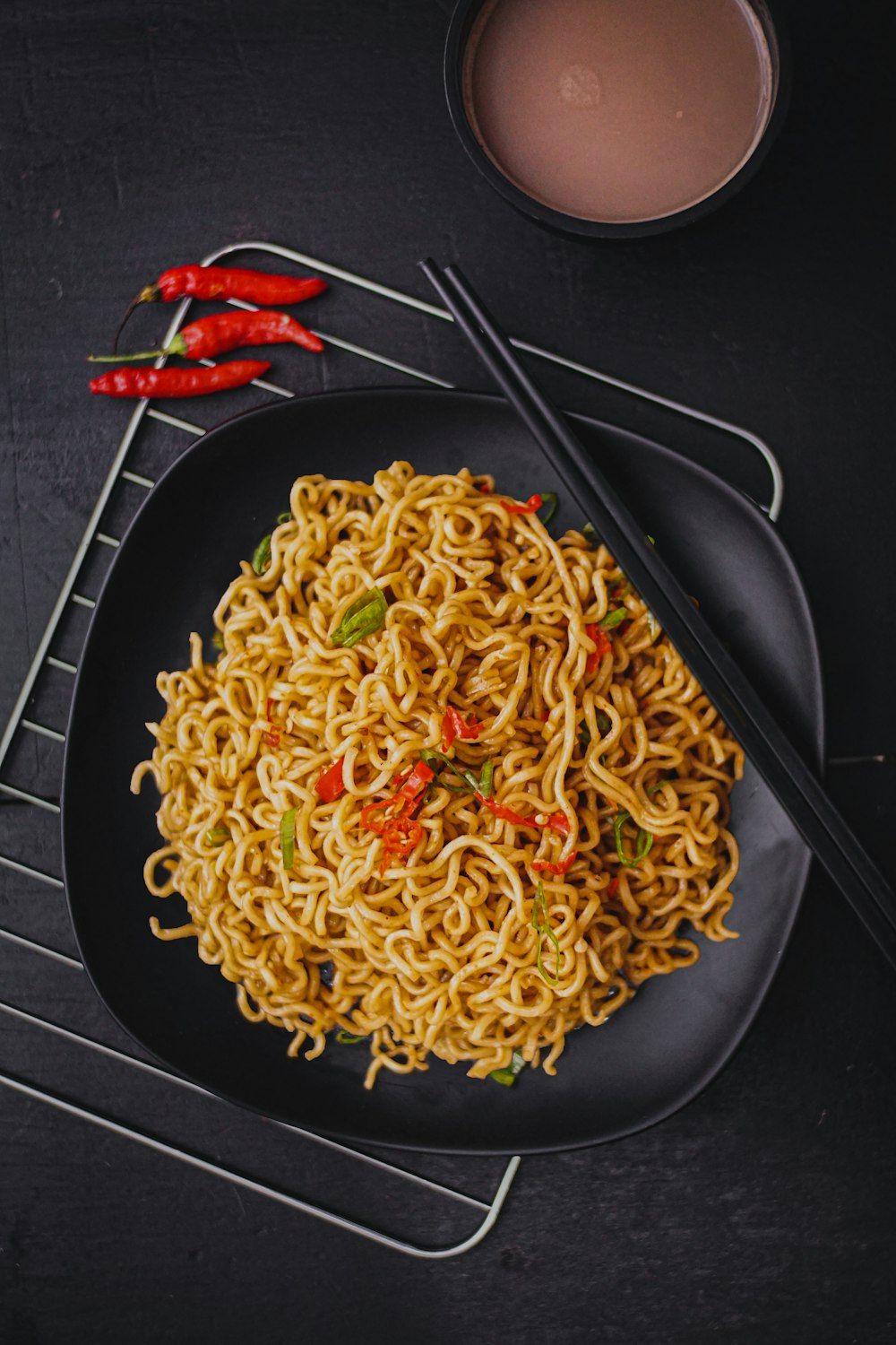A black bowl of noodles with red peppers and green onions. - Pasta