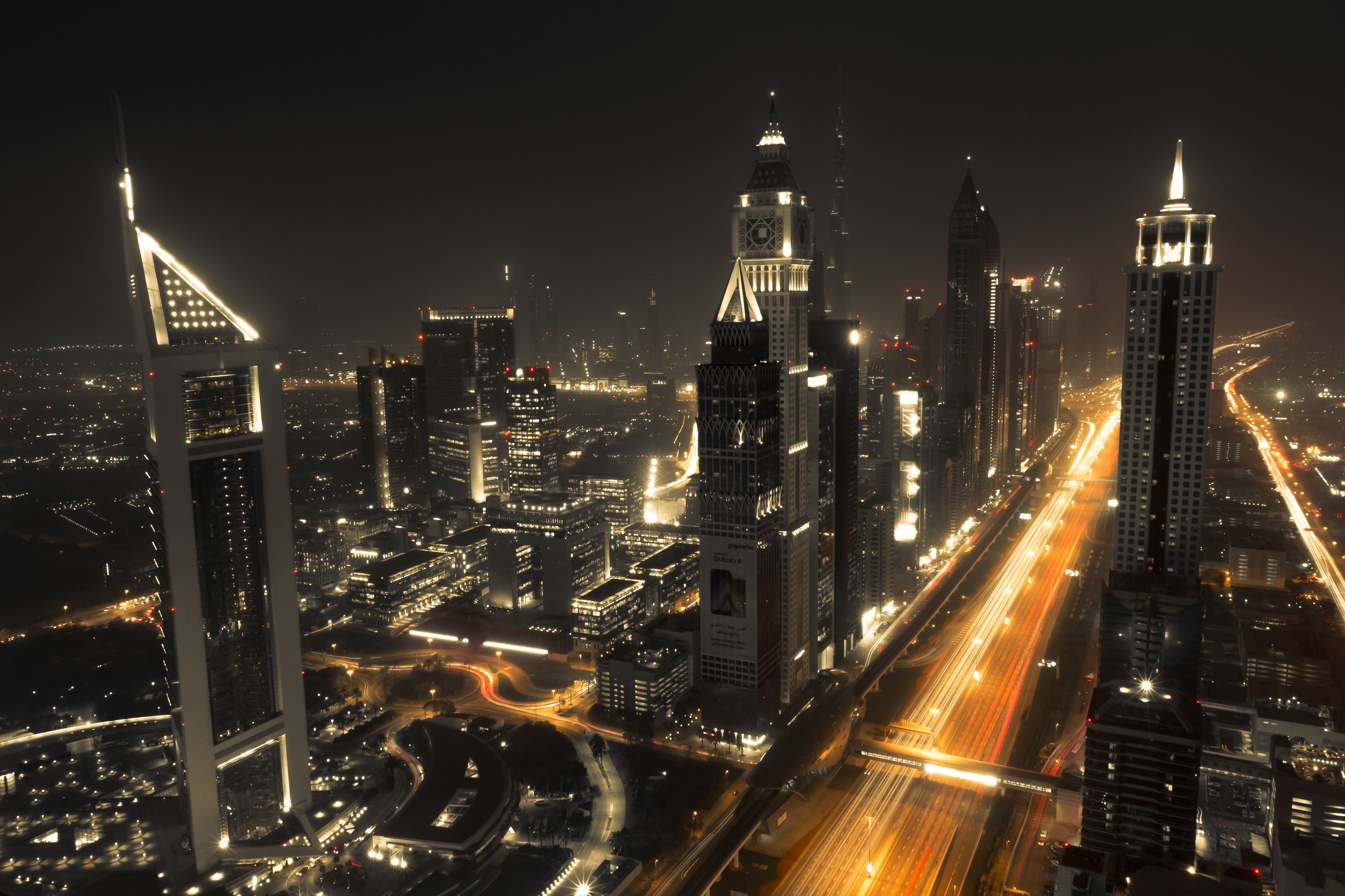 A nighttime view of the city of Dubai, with a long exposure of the highway in the foreground. - Dubai