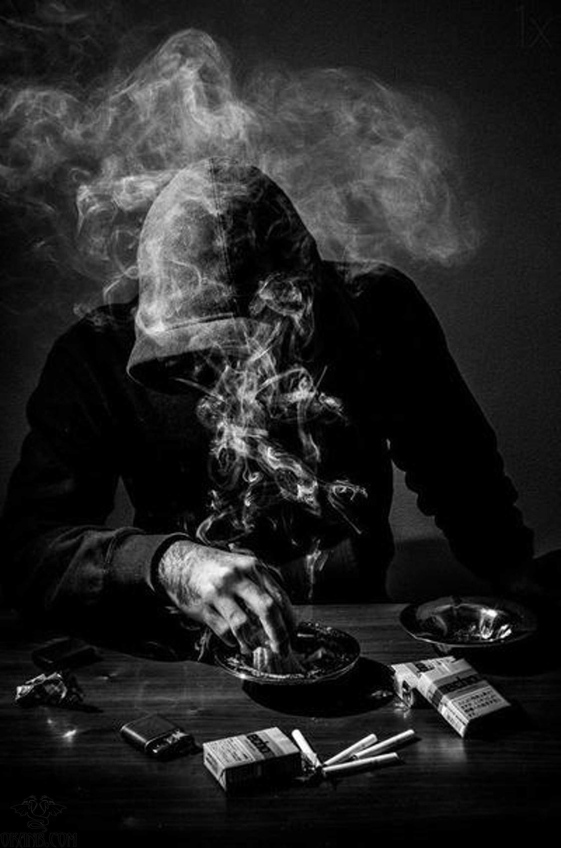 A hooded figure sits at a table, surrounded by cigarette smoke and ashtray - Gangster