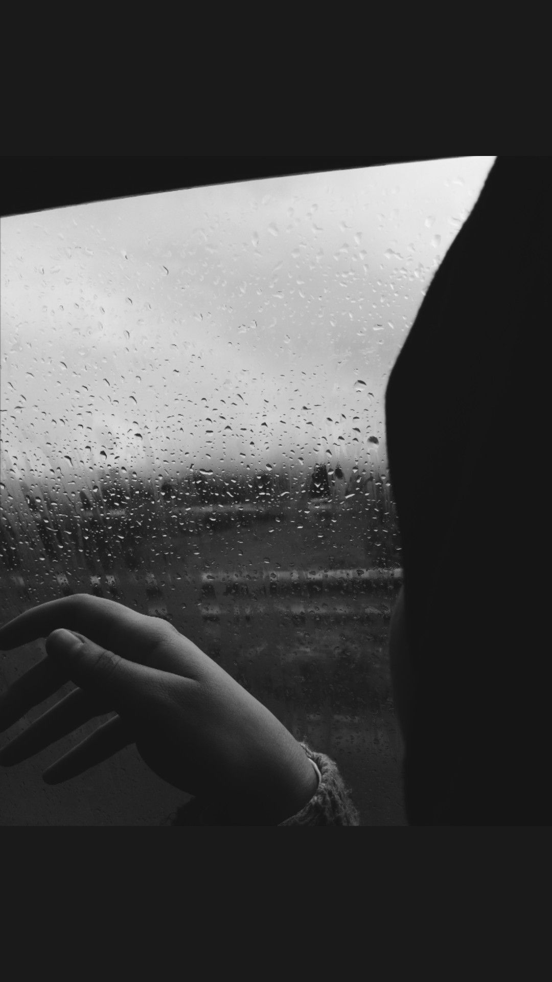 A person looking out a window with rain on it - Black and white