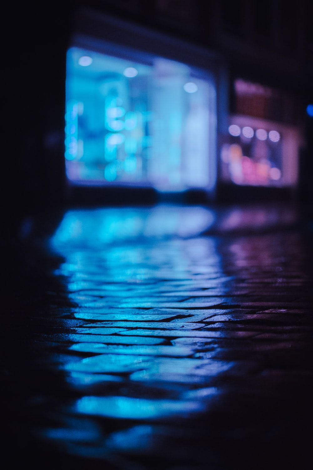 A wet street at night with blue lights reflecting on the pavement - Neon blue